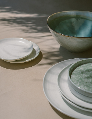 Stacked plates and bowls on a beige surface with shadows.