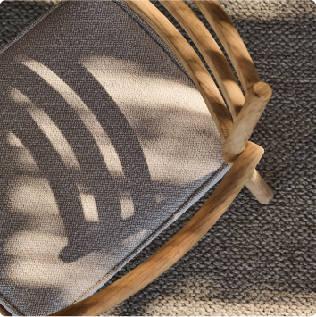 Close-up of a wooden chair with a fabric seat, placed on a textured carpet.