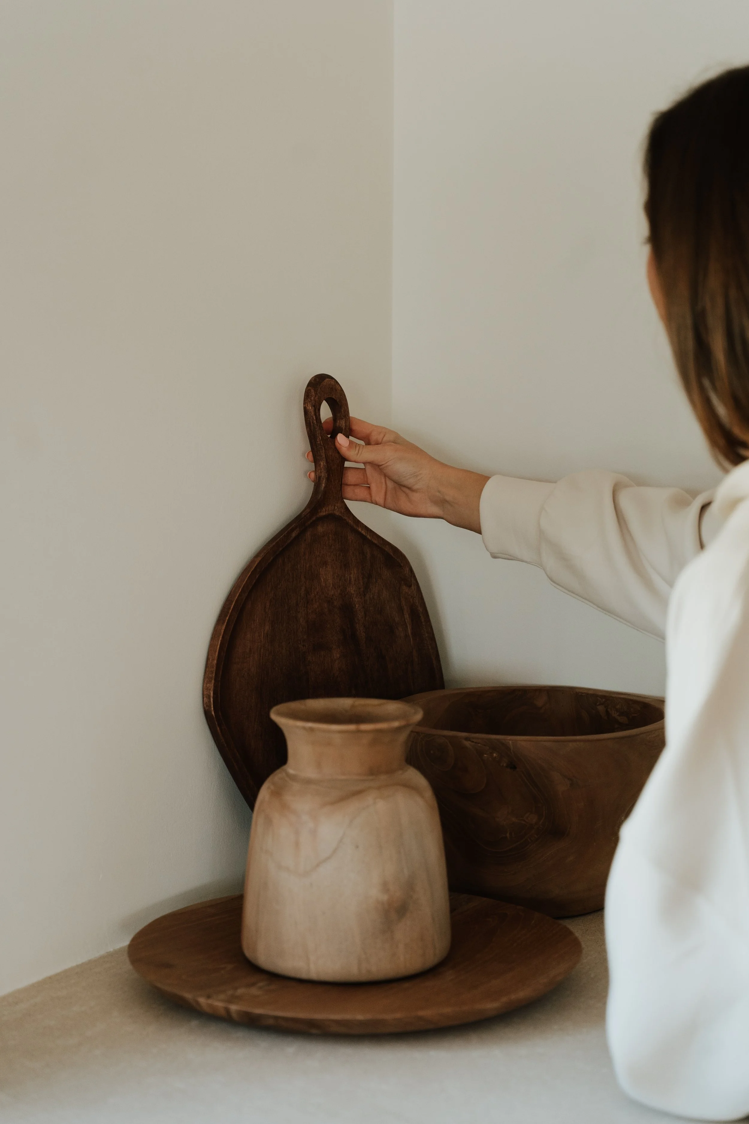 Person arranging wooden kitchenware on a beige surface, including a cutting board, a bowl, and a vase. We give advice to clients in interior , exterior and renovation projects