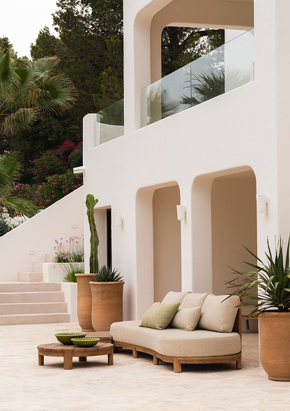 Modern white outdoor patio area with beige lounge sofa, potted plants, and a glass-paneled balcony