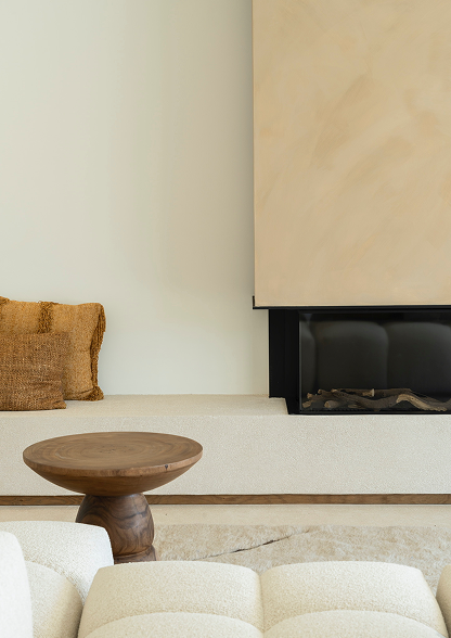 Living room with a brown cushion on a beige sofa, a small wooden round coffee table, and a fireplace with a beige wall and black frame.
