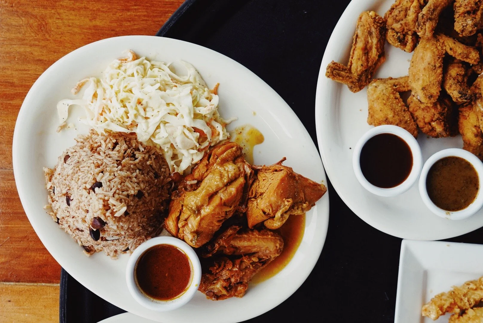 Plate of rice and beans, coleslaw, and chicken in sauce with fried chicken wings on a side