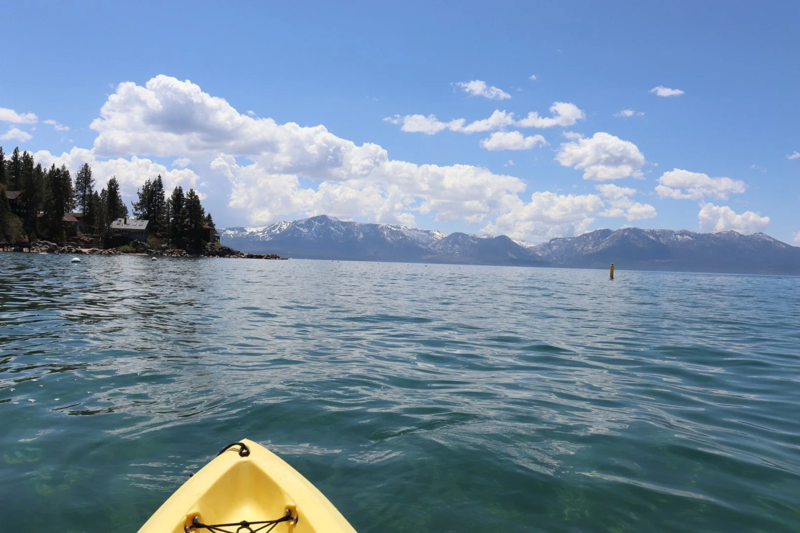 View from a yellow kayak on a lake with mountains in the background under a partly cloudy sky.