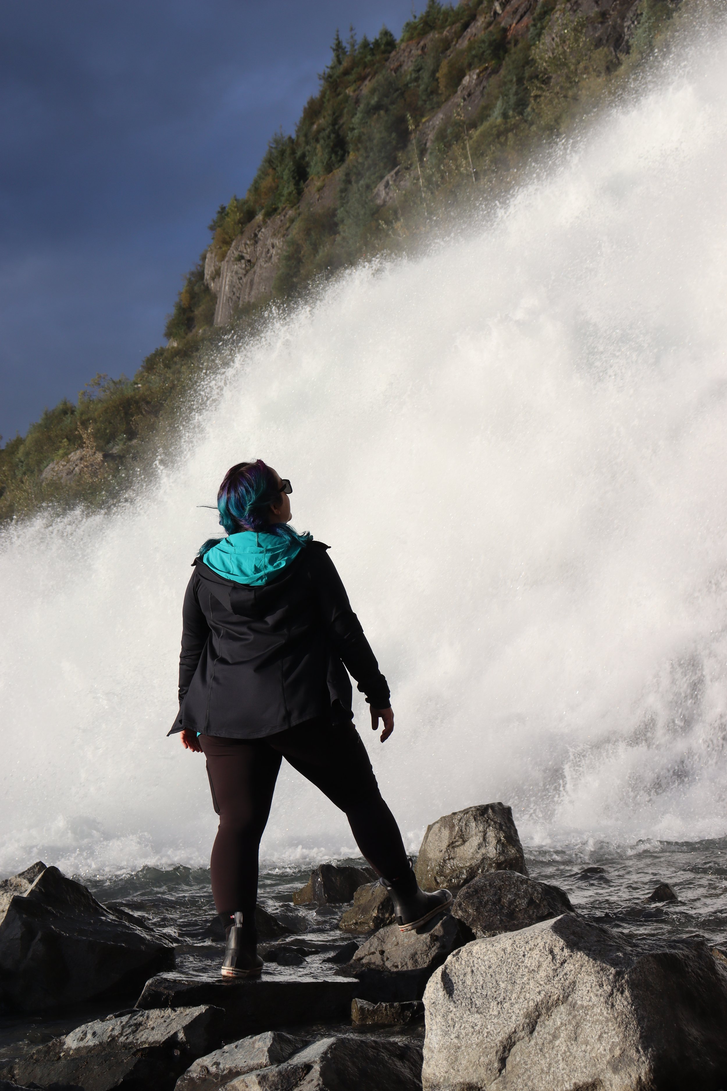 A person standing on rocks near a waterfall or rapid, looking at the cascading water. Mendenhall Glacier area, Juneau Alaska