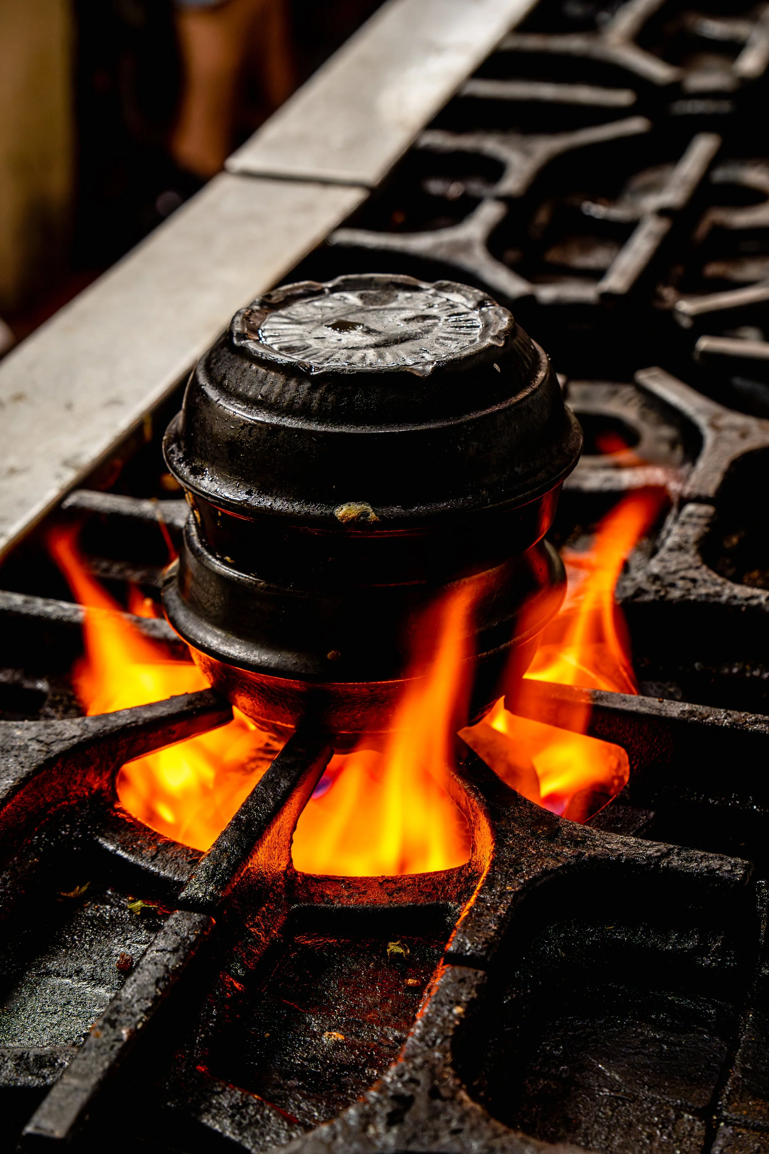 A close-up of a gas stove with burning flames and a blackened pot on top.