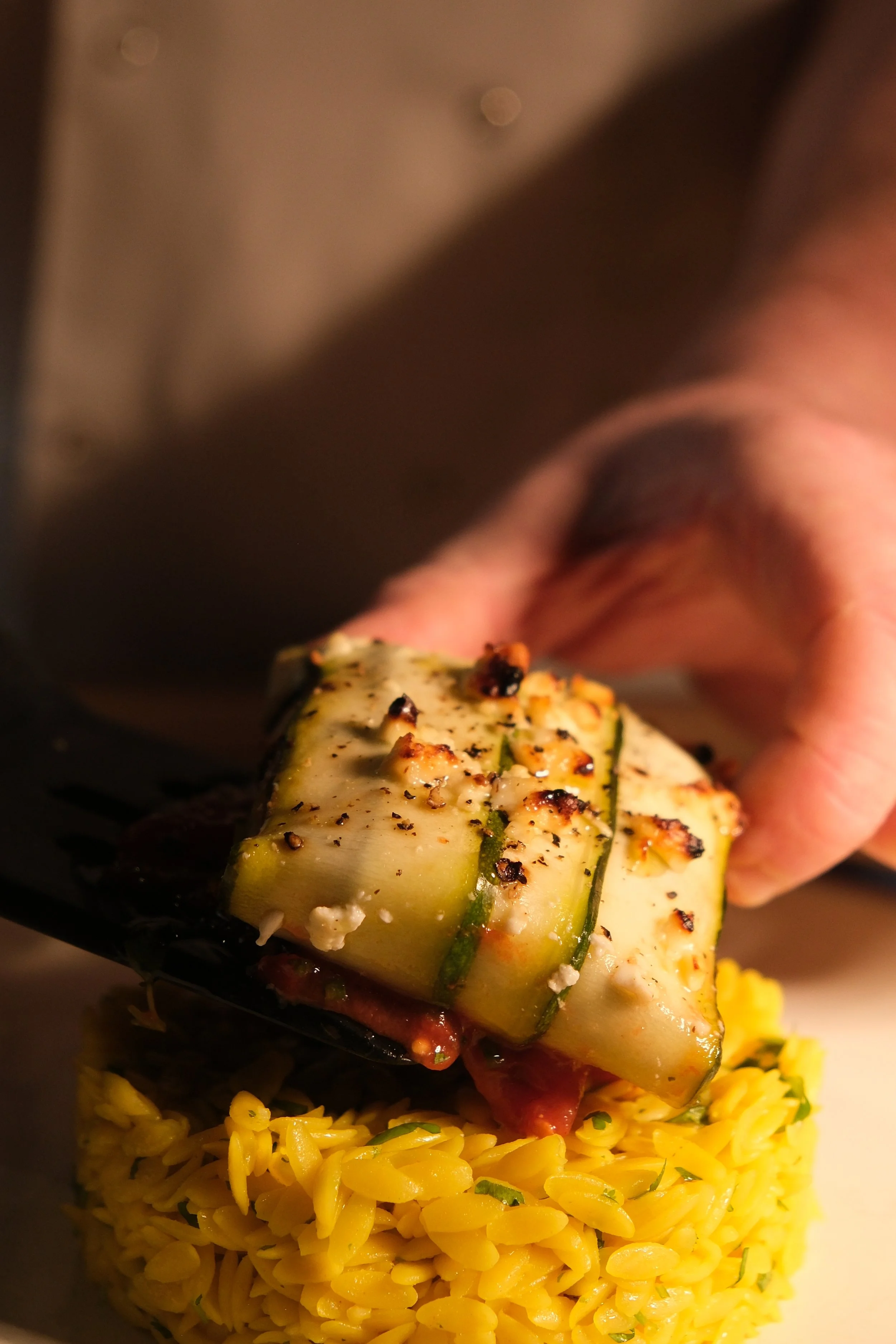 Close-up of a hand placing a grilled zucchini slice on a bed of yellow rice.