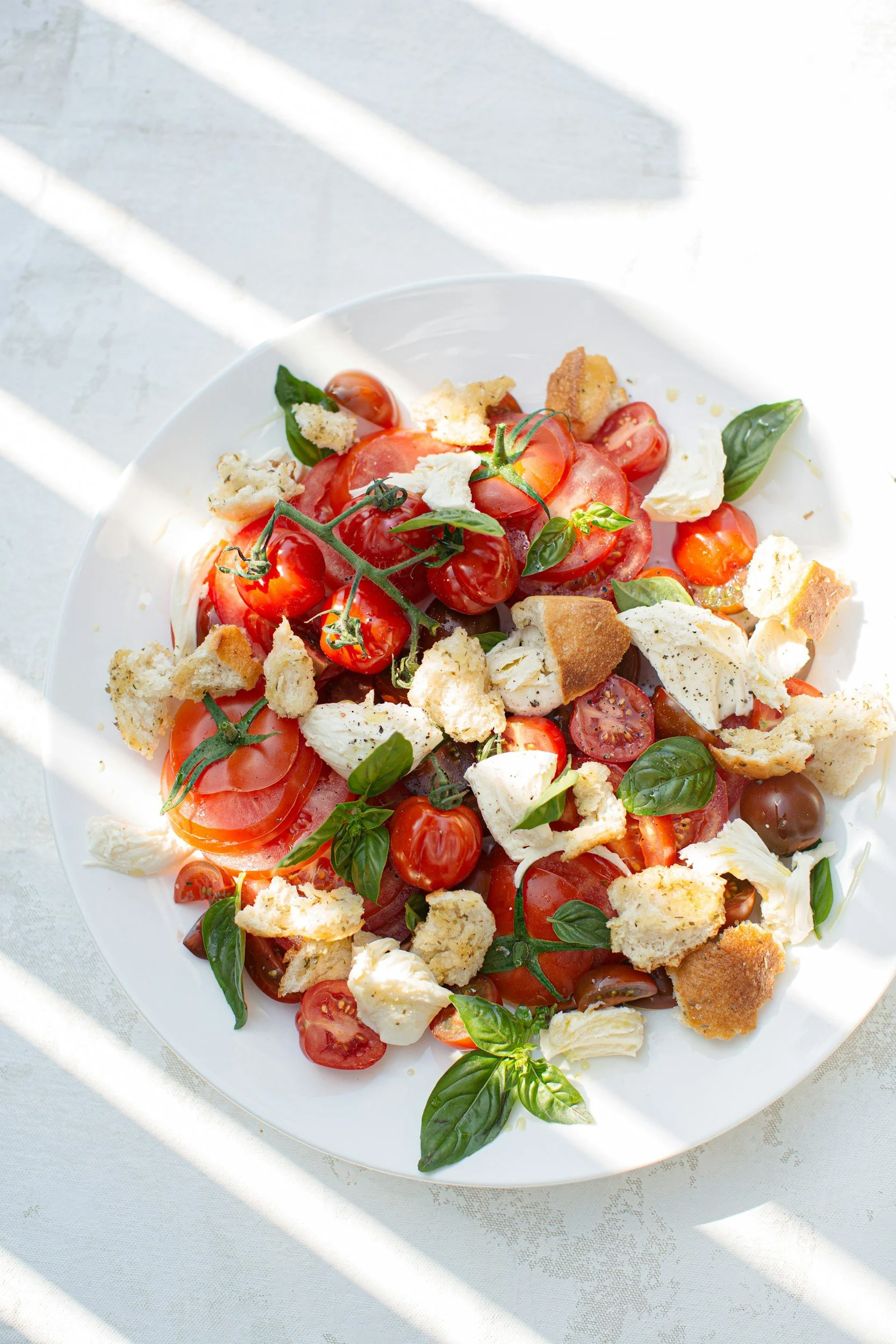 A plate of Caprese salad with cherry tomatoes, fresh mozzarella, basil leaves, and bread croutons.
