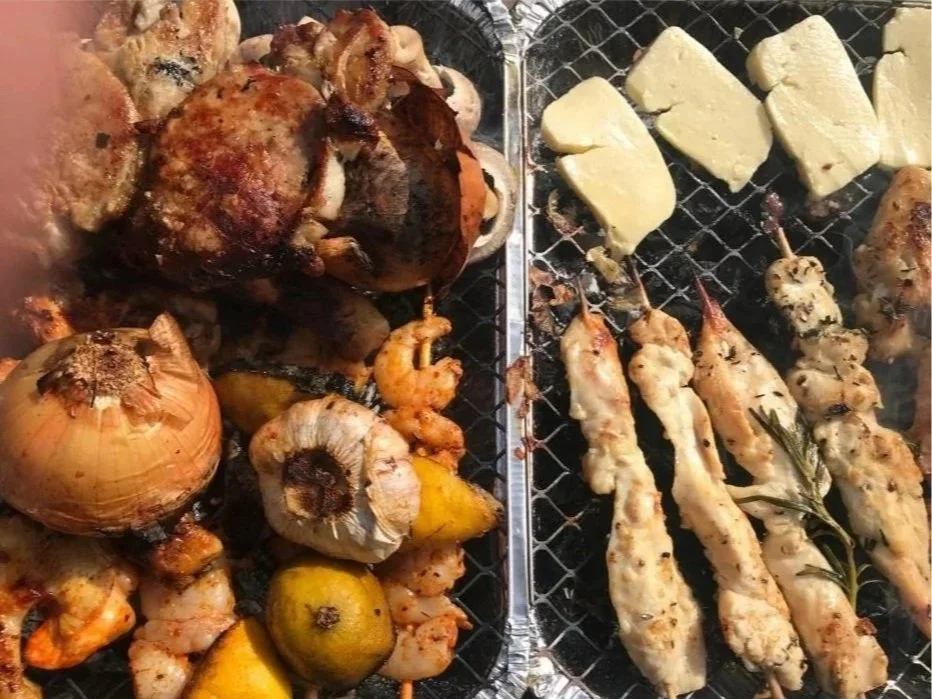 Assorted grilled foods including chicken, shrimp, onion, lemon, cheese, and skewers of chicken with herbs.
