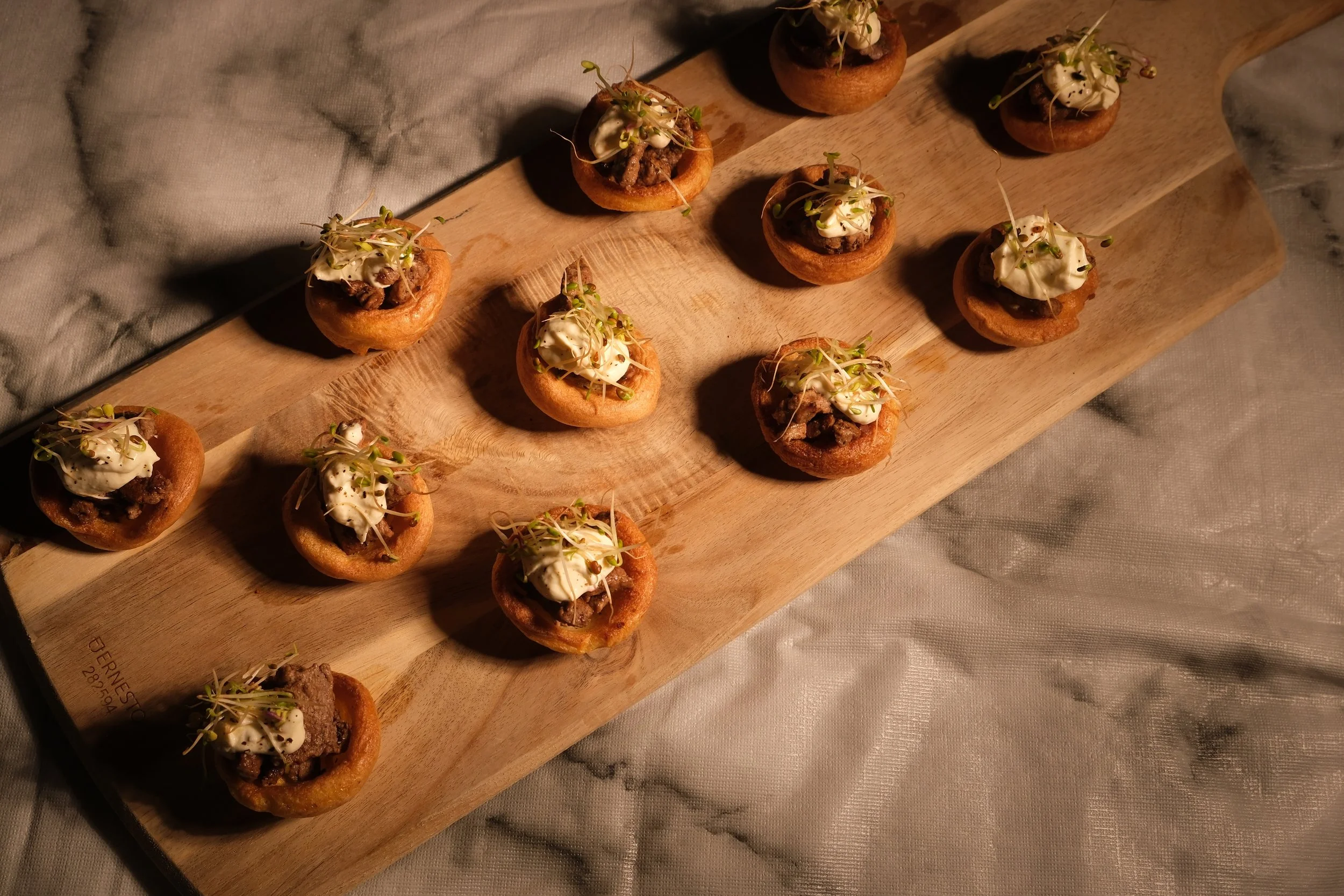 Appetizer bites with a savory filling topped with microgreen sprouts on a wooden board.