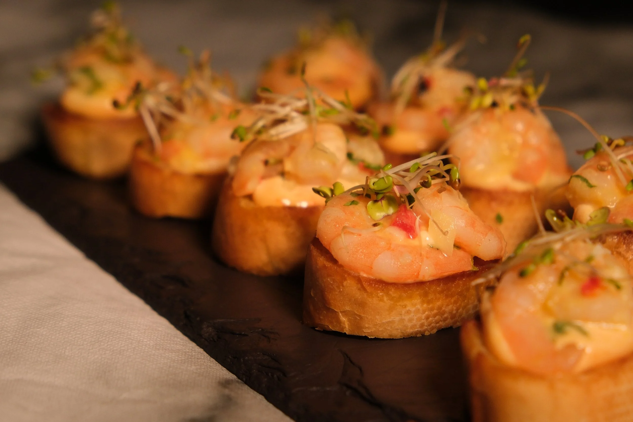 Shrimp canapé appetizers with microgreens on a dark serving board.