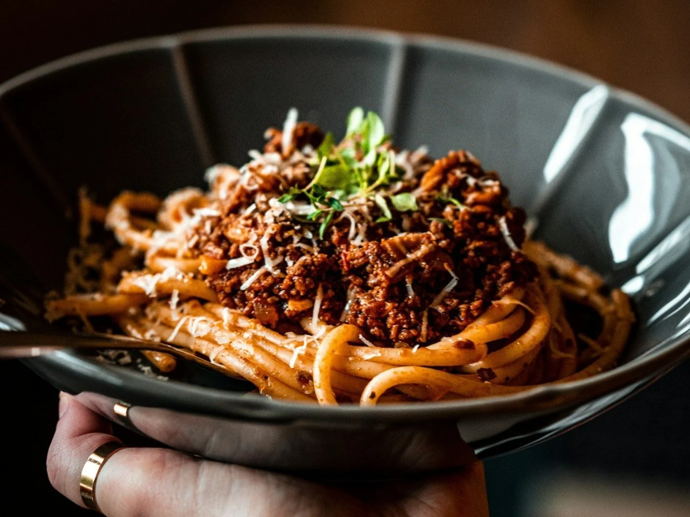 Plate of spaghetti with meat sauce, grated cheese, and fresh herbs.