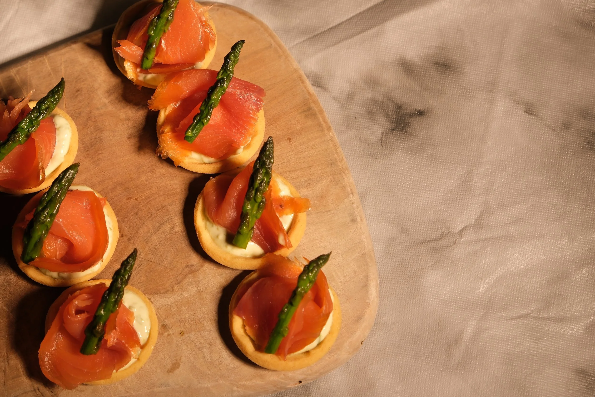 Close-up of smoked salmon and asparagus appetizers on a wooden tray, served on small round crackers with a cream cheese spread.