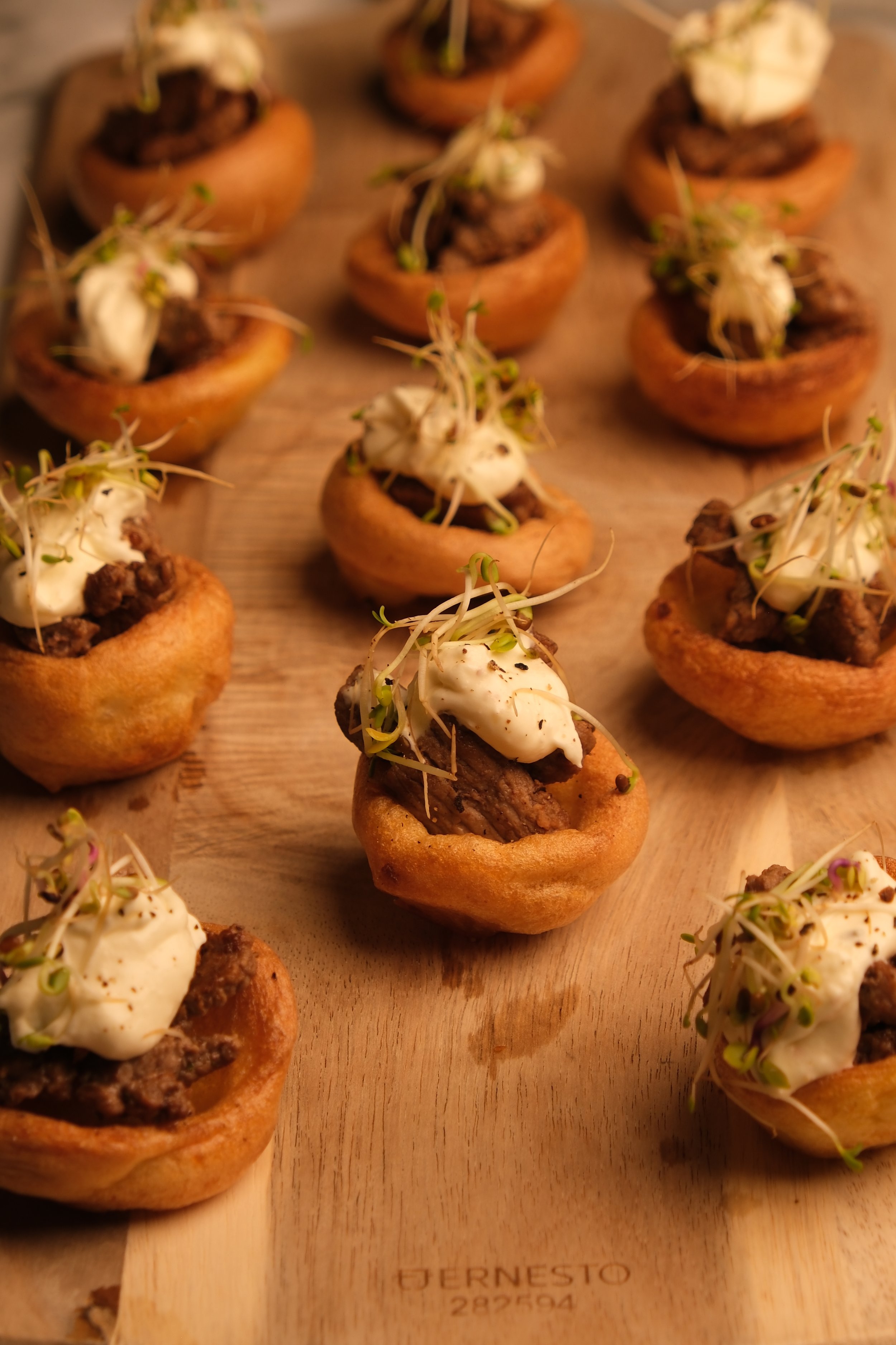 Miniature pastries topped with dollops of cream and sprouts on a wooden serving board.