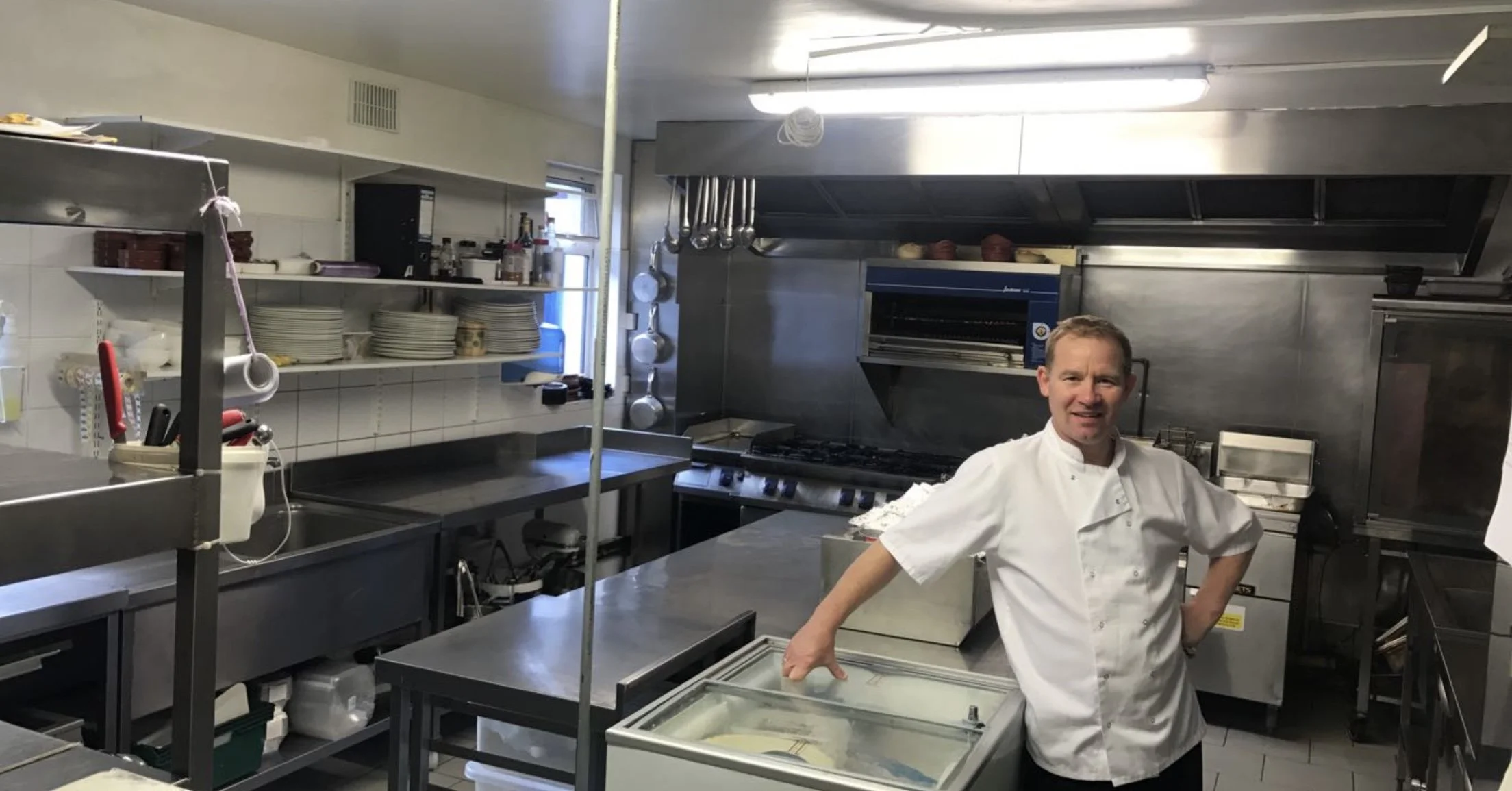 Chef standing in a professional kitchen with stainless steel countertops, stove, and shelves filled with dishes and kitchen tools in Westmeath.