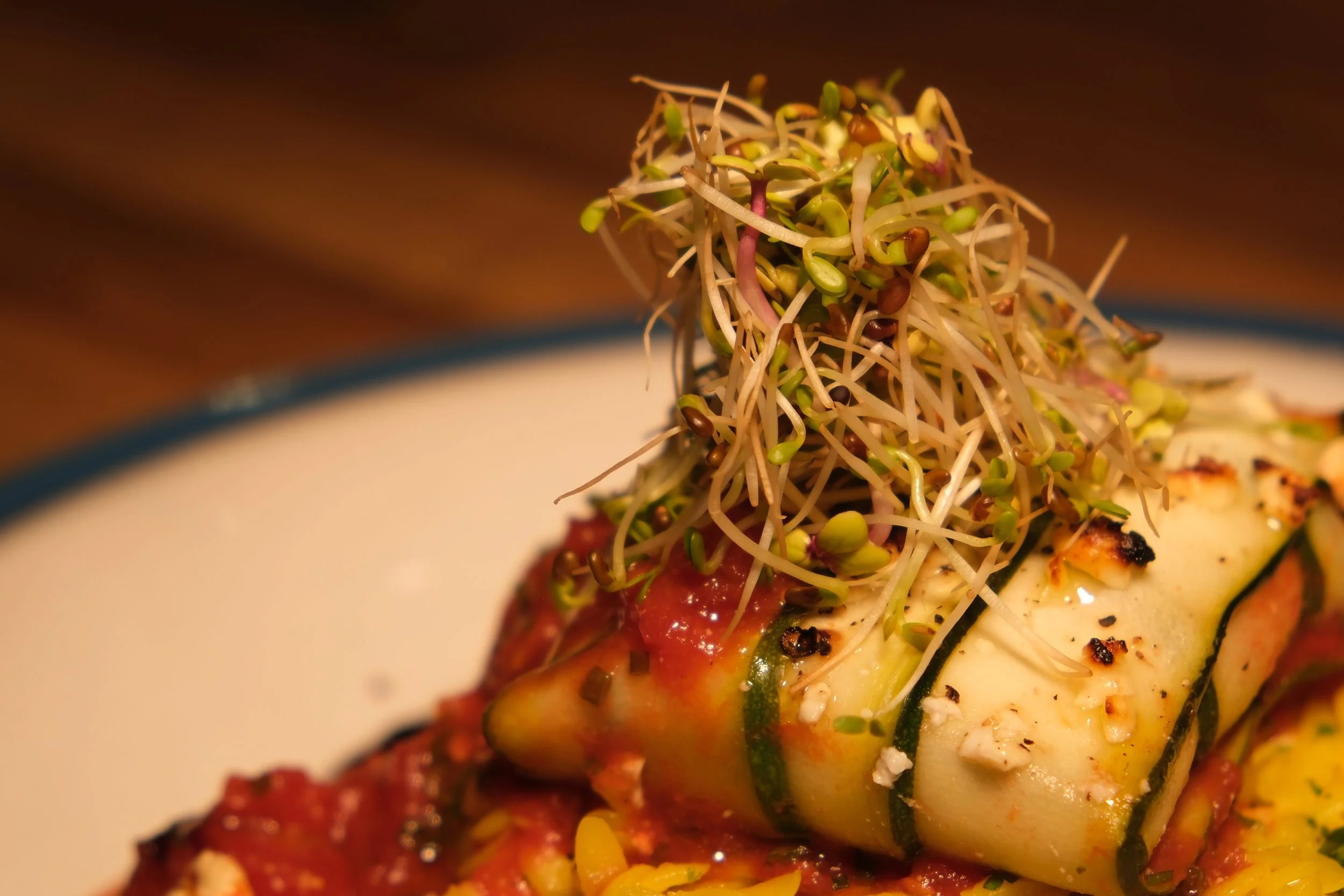 Close-up of a plate with grilled zucchini topped with microgreens and sauce.