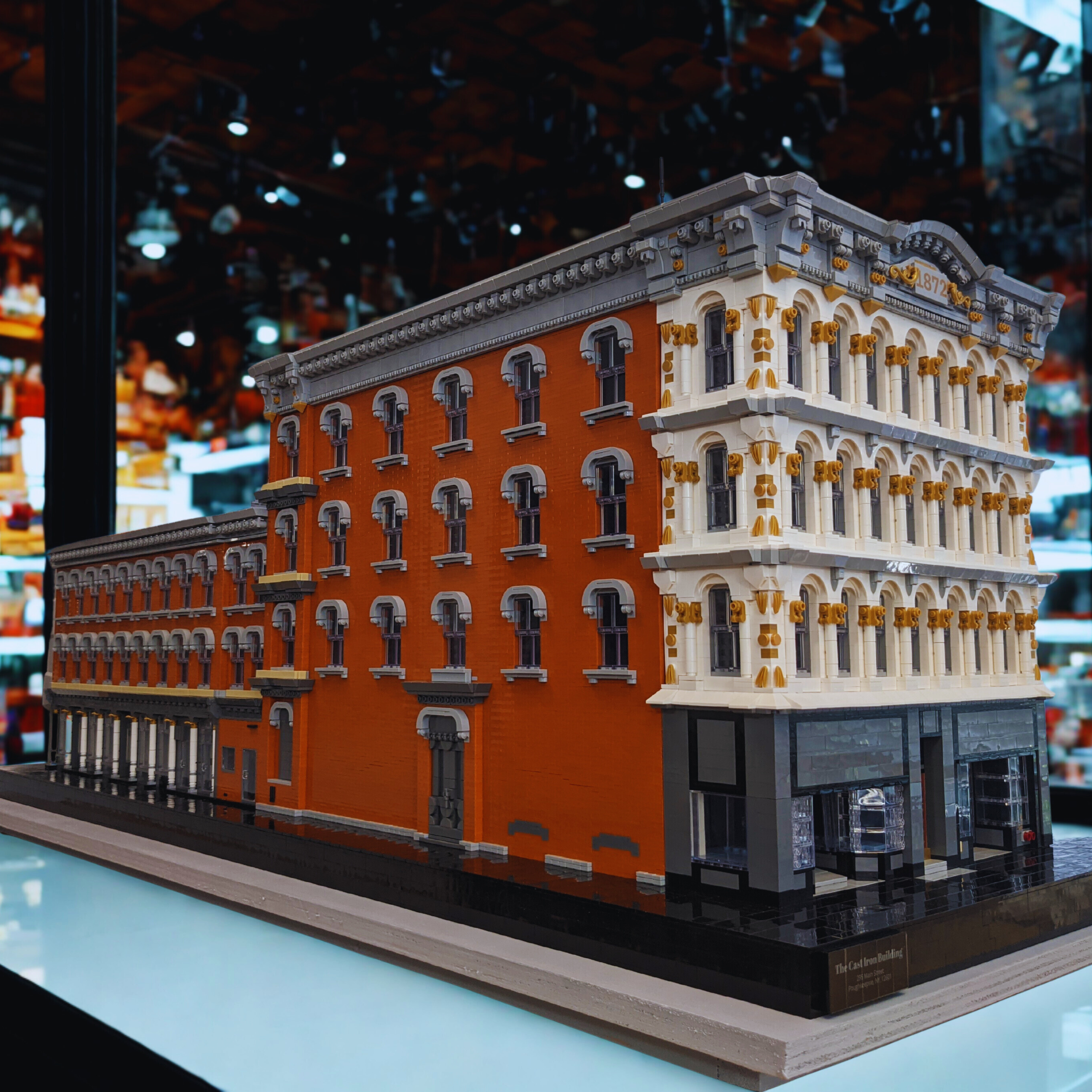 Lego model of a historic brick building with ornate architectural details, large windows, and a black storefront on the ground level.