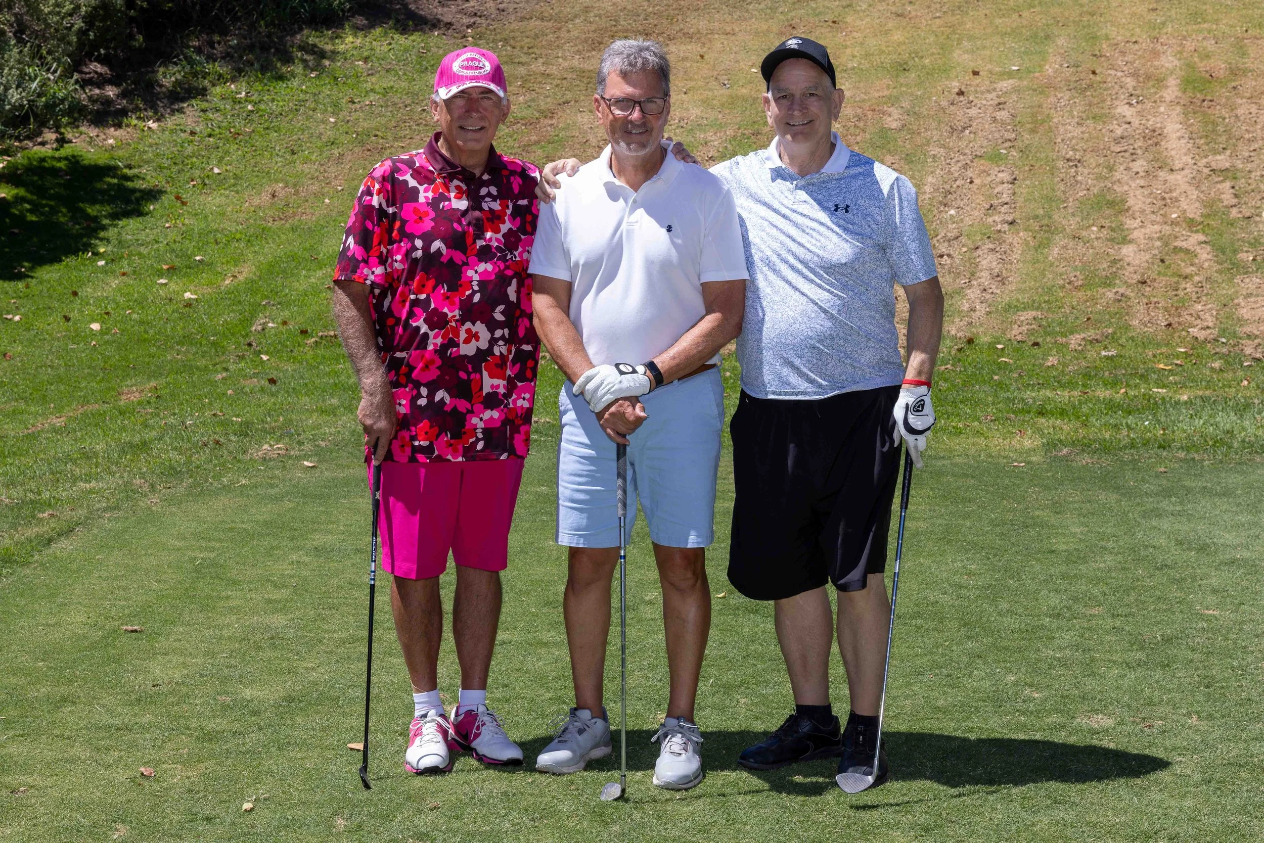 Three men standing together on a golf course, posing with golf clubs and smiling at the camera.