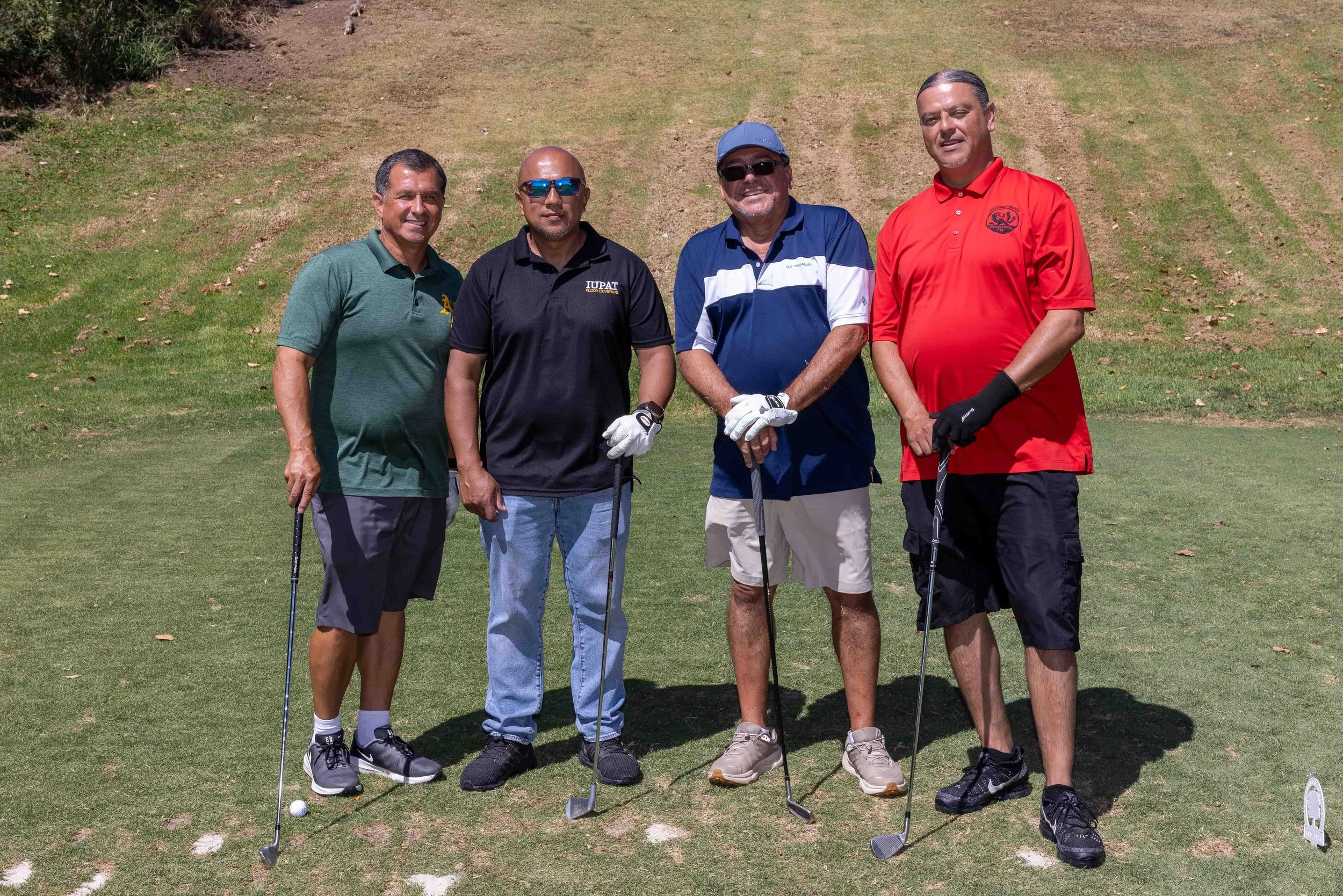 Four men standing together on a golf course, holding golf clubs, posing for a photo.