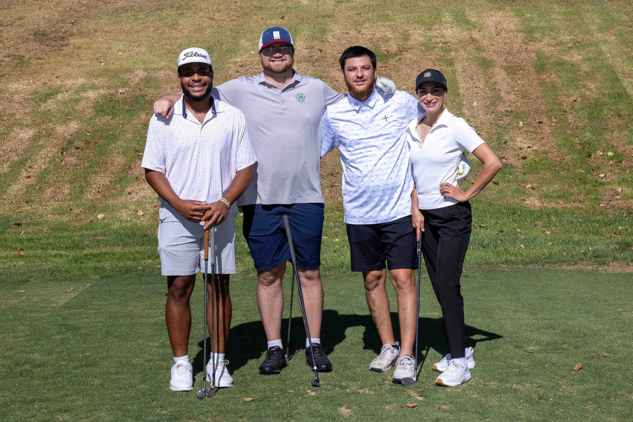 Group of four friends on a golf course, smiling, with golf clubs, standing on grass.