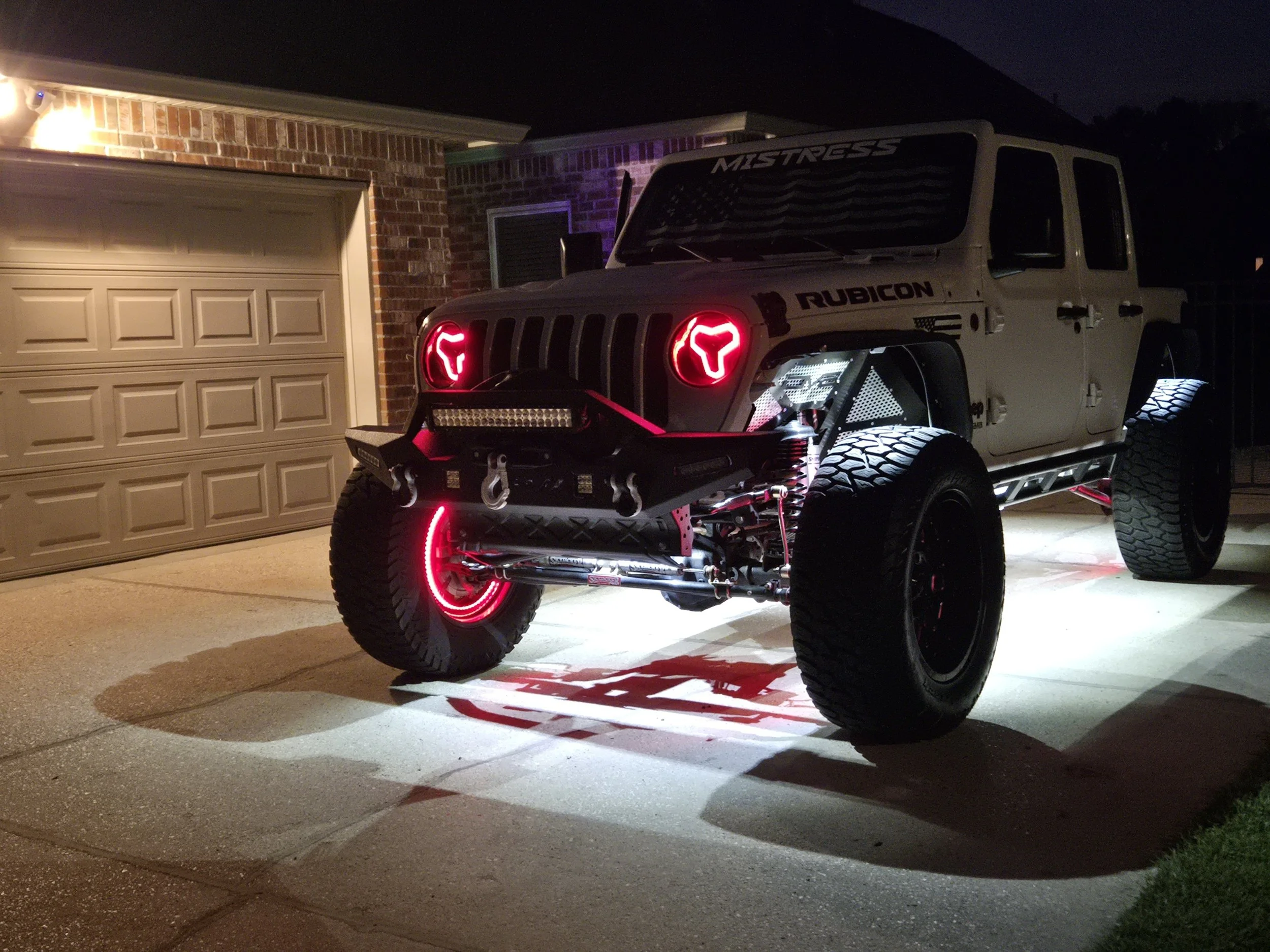 A custom off-road Jeep Rubicon with neon red and white lights parked in a driveway at night.