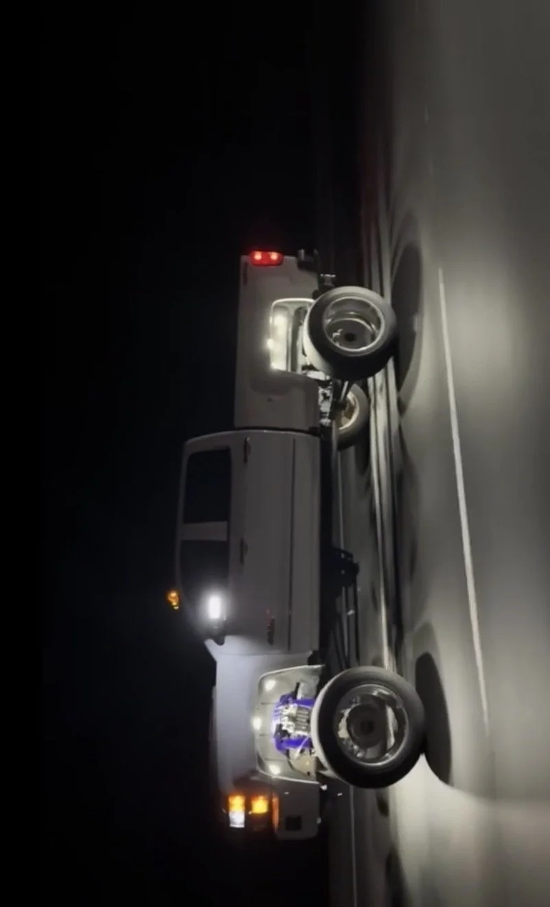 A pickup truck is towing a small trailer on a dark road at night.
