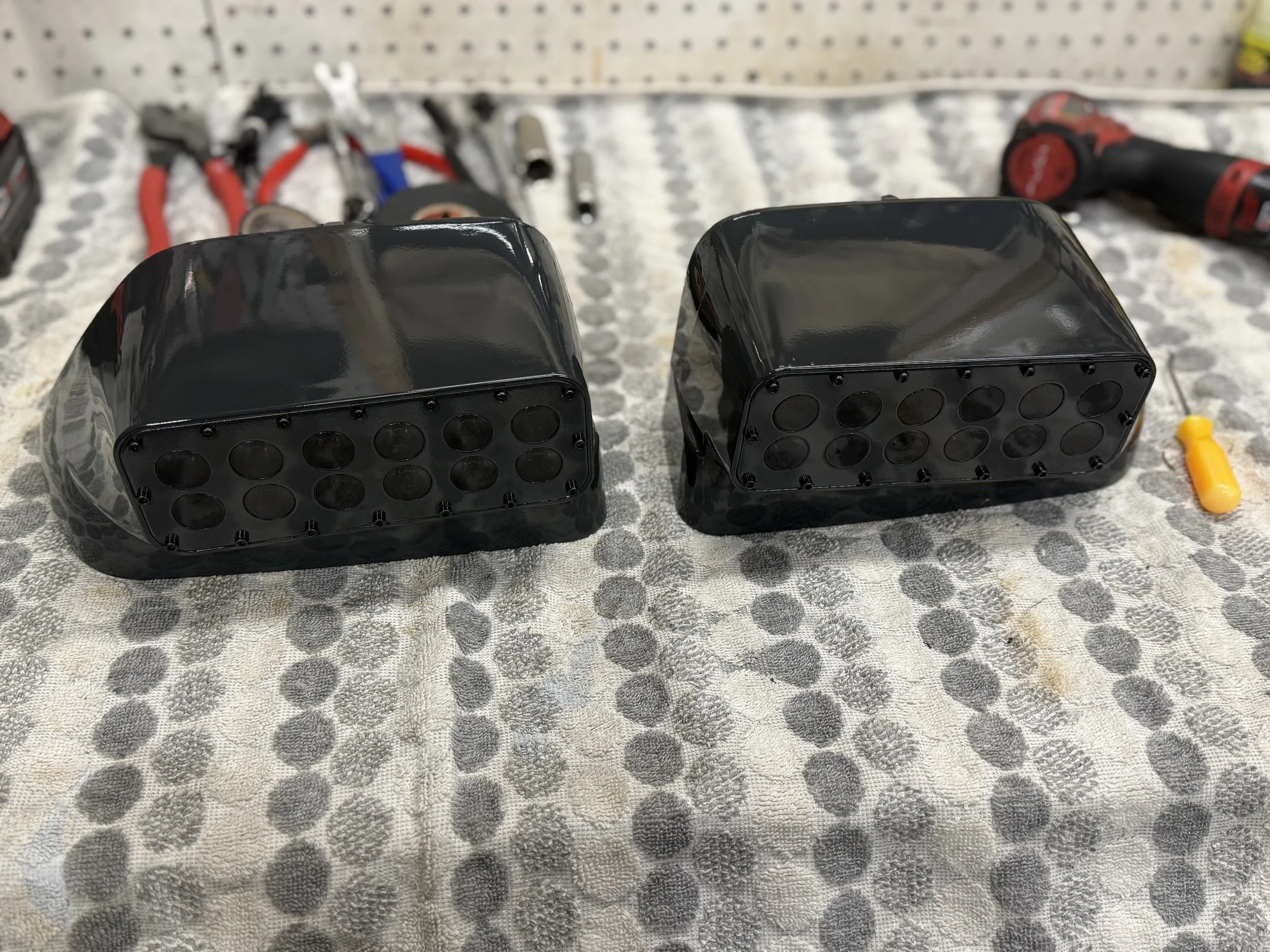 Two black LED tail lights for a vehicle placed on a workbench with tools in the background.