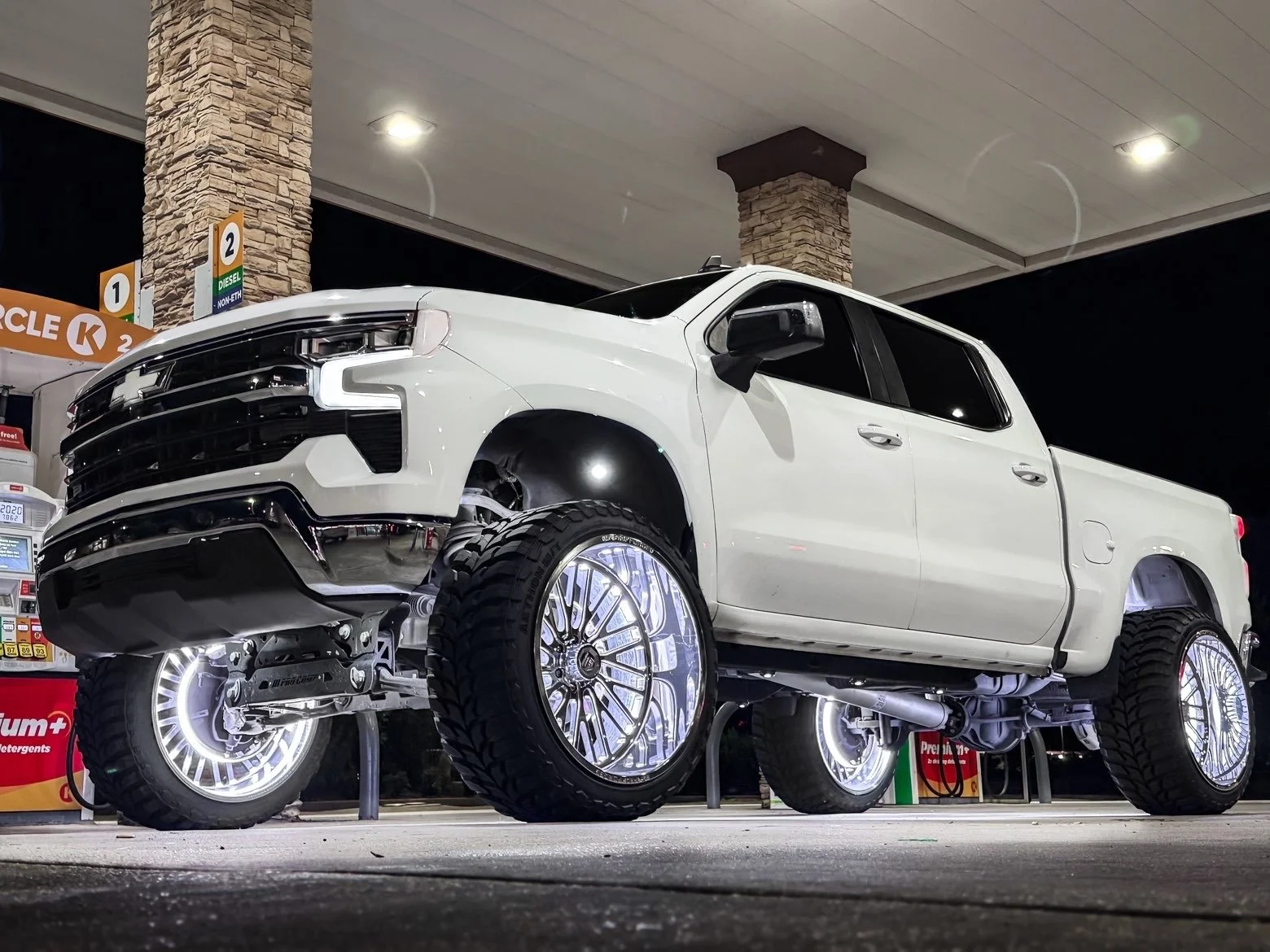 A white pickup truck with illuminated rims parked at a gas station at night.