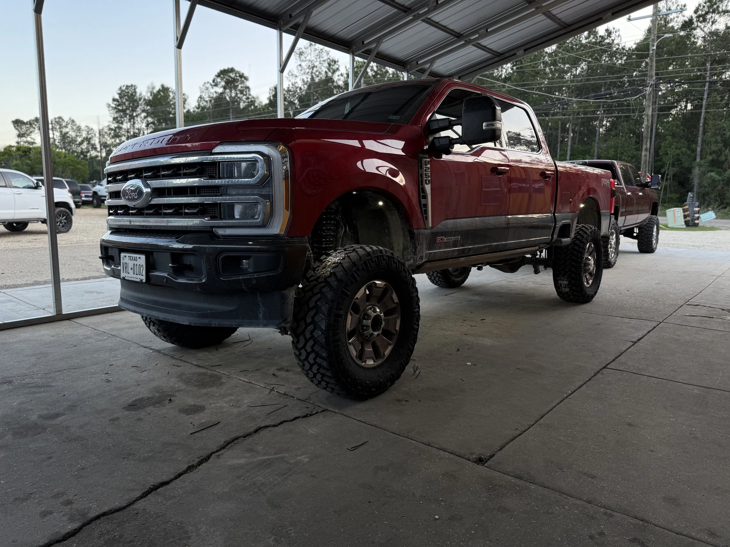 Red Ford Super Duty pickup truck with lifted suspension and off-road tires parked under a canopy.
