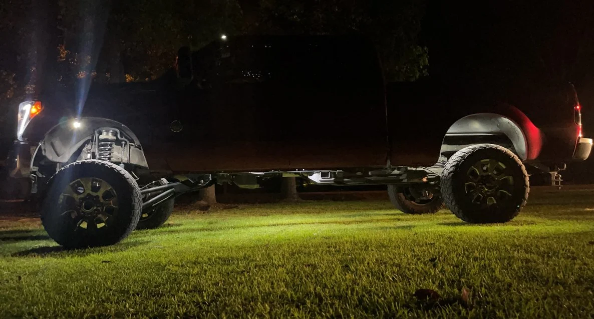 Black pickup truck parked on grass at night with illuminated headlights.