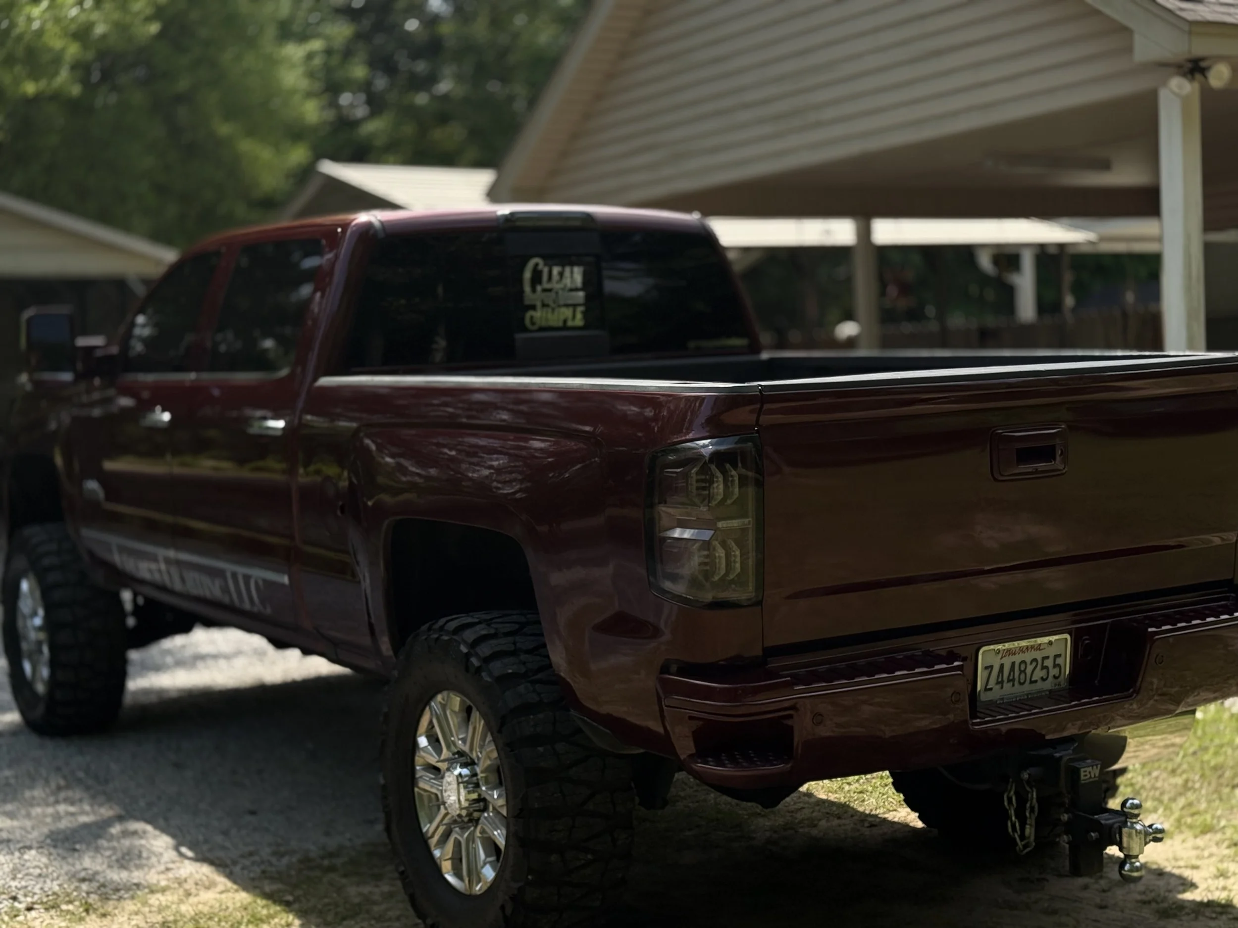 Maroon pickup truck parked on a gravel driveway with a house in the background.