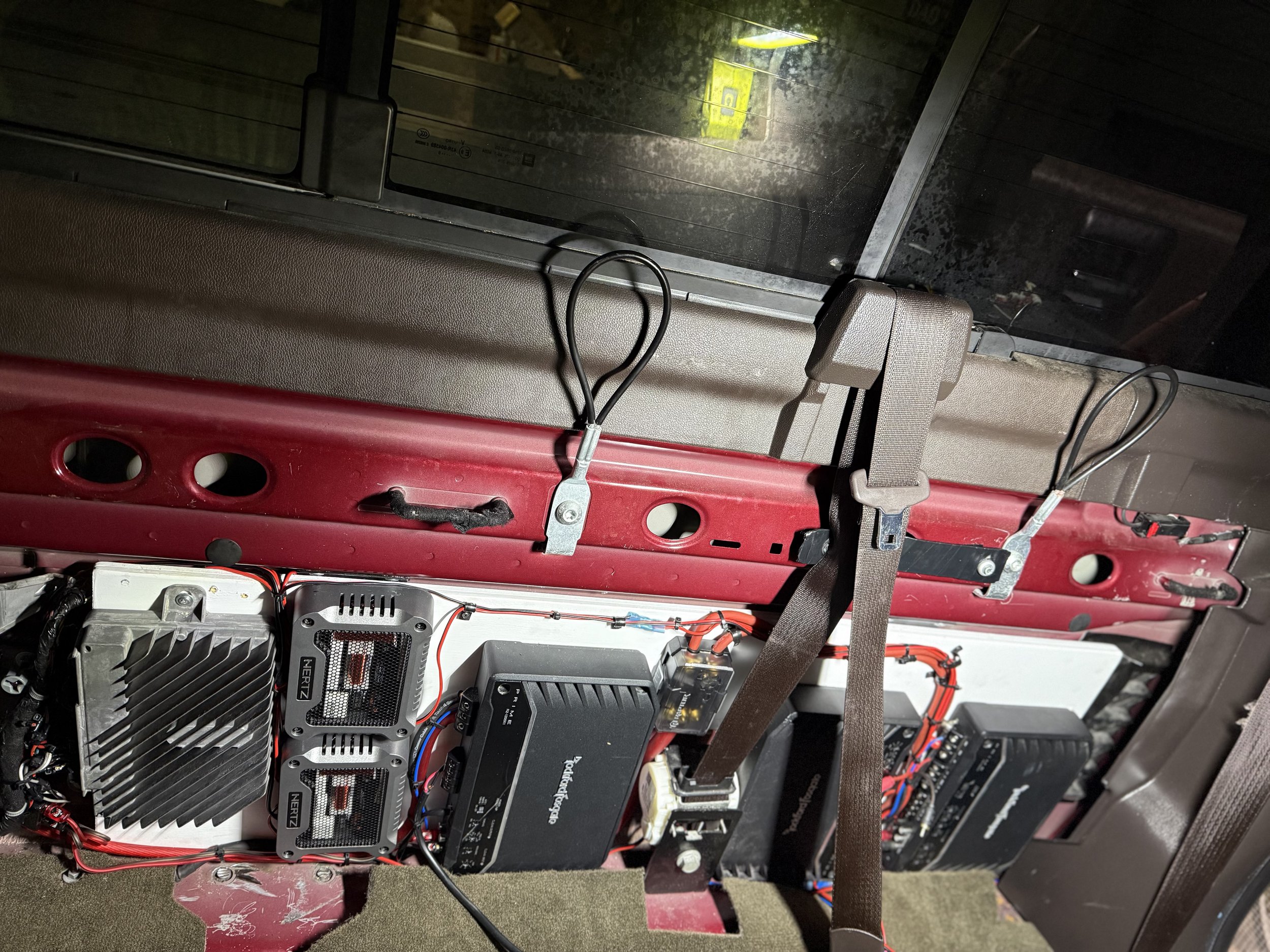 The image shows the interior of a vehicle with various electronic components and wiring, mounted on the floor behind the dashboard, including a black electronic box, circuit boards, and wiring harnesses.