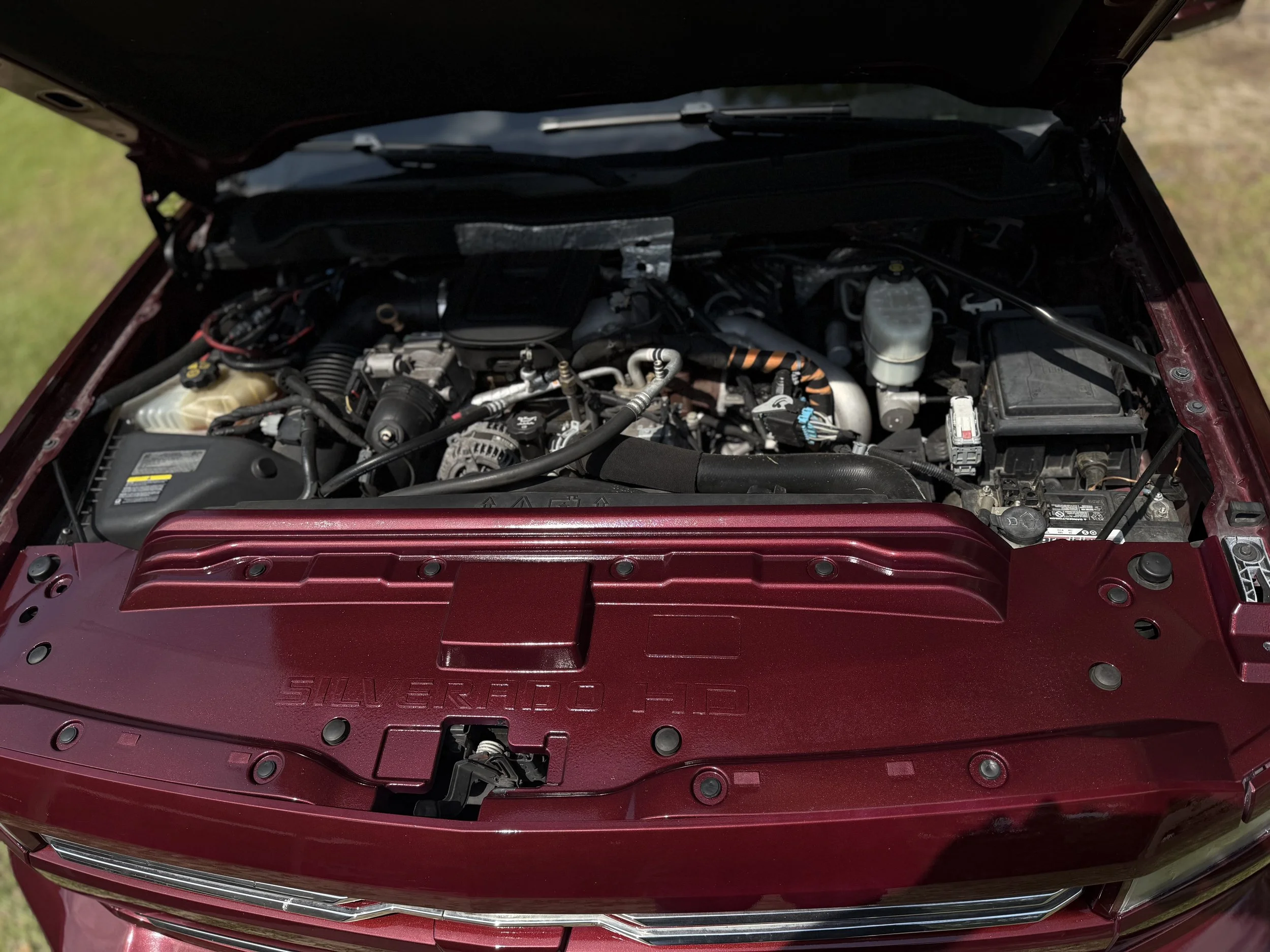Open hood of a car revealing a clean engine bay with a maroon engine cover labeled 'SILVERADO 1-TD'.