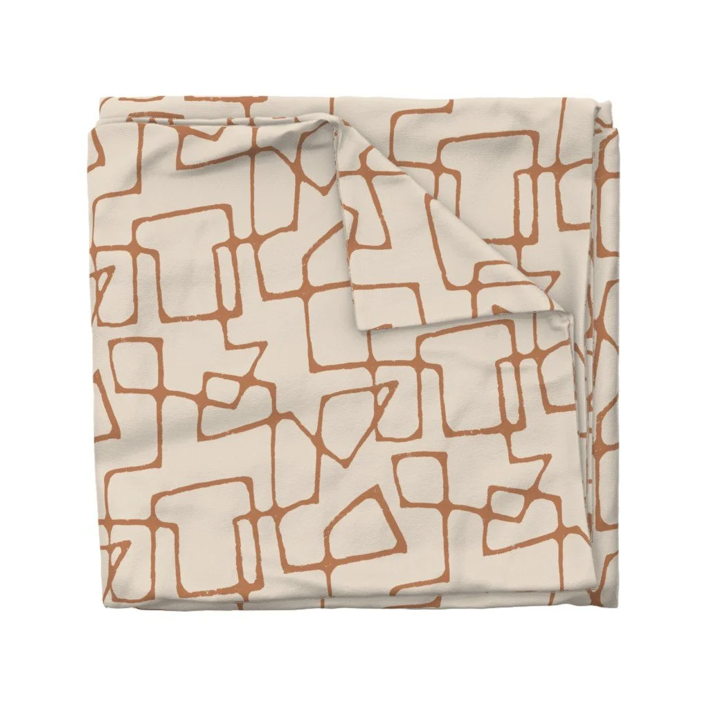 Folded fabric with a geometric pattern of irregular orange-brown lines on an off-white background.