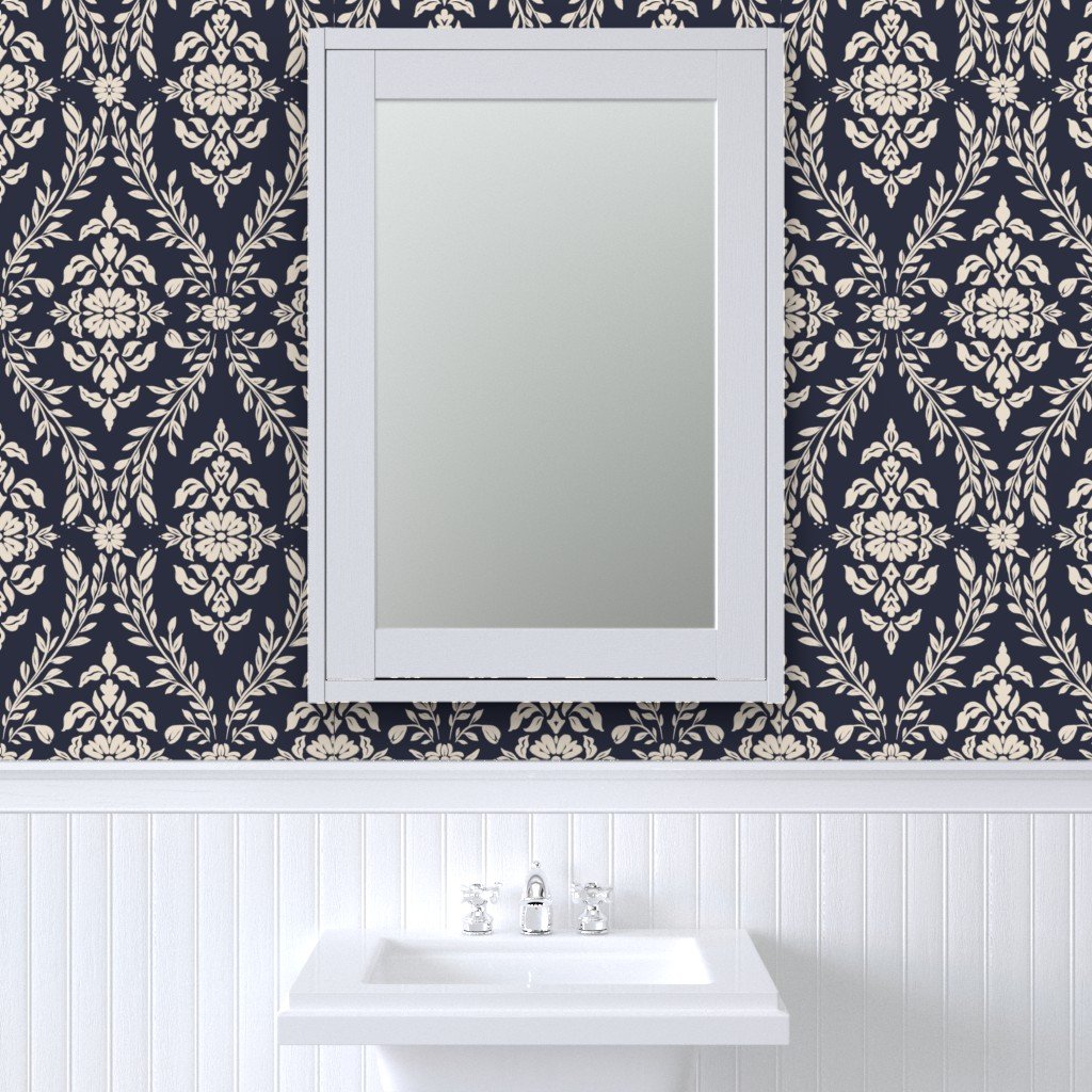 A bathroom wall with dark blue wallpaper featuring a white floral pattern and a white framed mirror above a small white sink with a silver faucet.