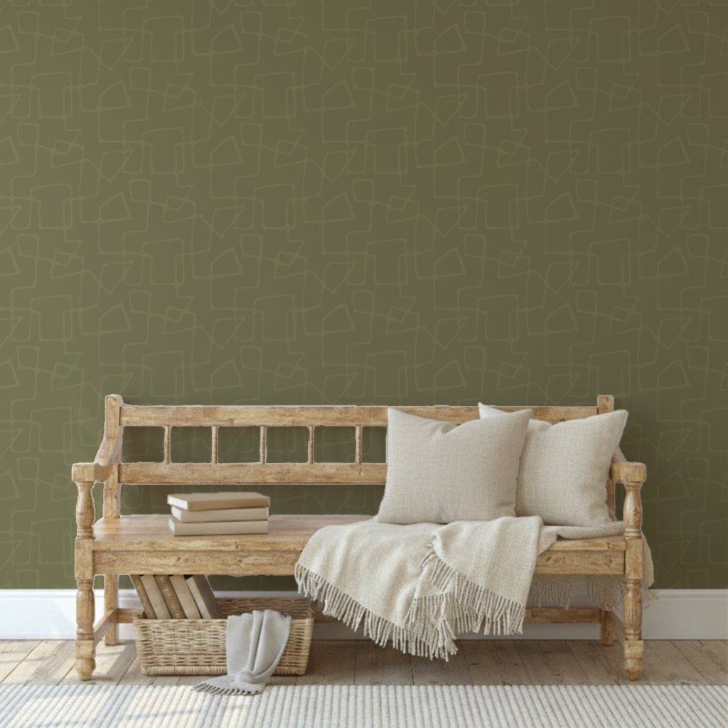 Wooden bench with three beige cushions and a cream throw blanket, books on the side, a wicker basket with a blanket underneath, against a tone-on-tone green patterned wallpaper.