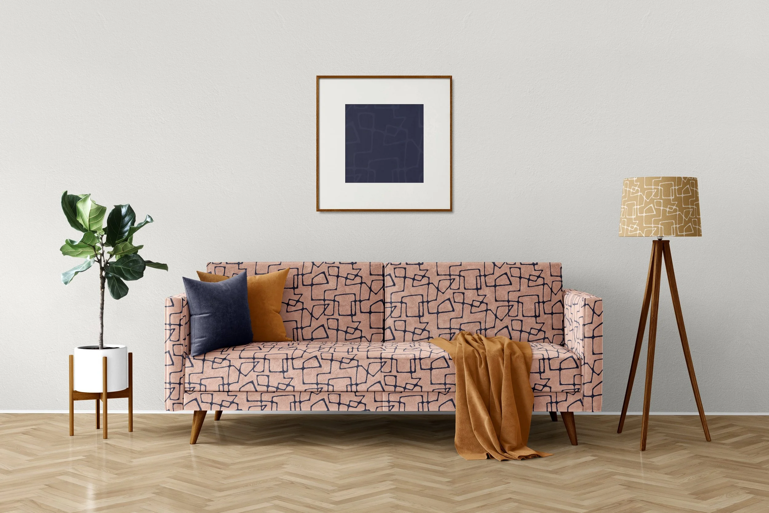 A living room with a gray wall, featuring a mid-century modern fabric couch with a pattern of indigo lines on a deep pink background, with navy and terracotta pillows, a terracotta throw blanket, a tall plant on the left, and a floor lamp opposite