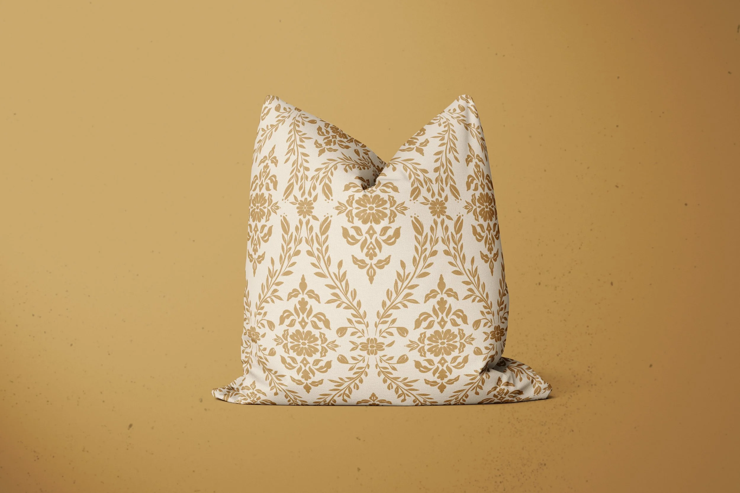 A single decorative pillow made with fabric with a floral damask pattern in deep yellow on a sand-colored background.  The pillow itself is on a coordinating yellow ochre background.