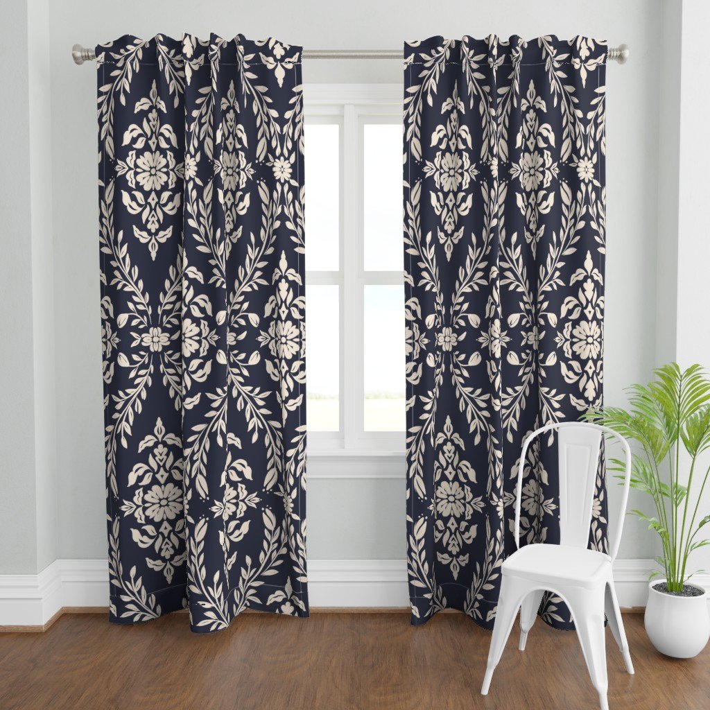 Decorative navy blue curtains with an off-white floral damask pattern hanging in front of a window in a room with wooden flooring, a white chair, and a potted green plant.
