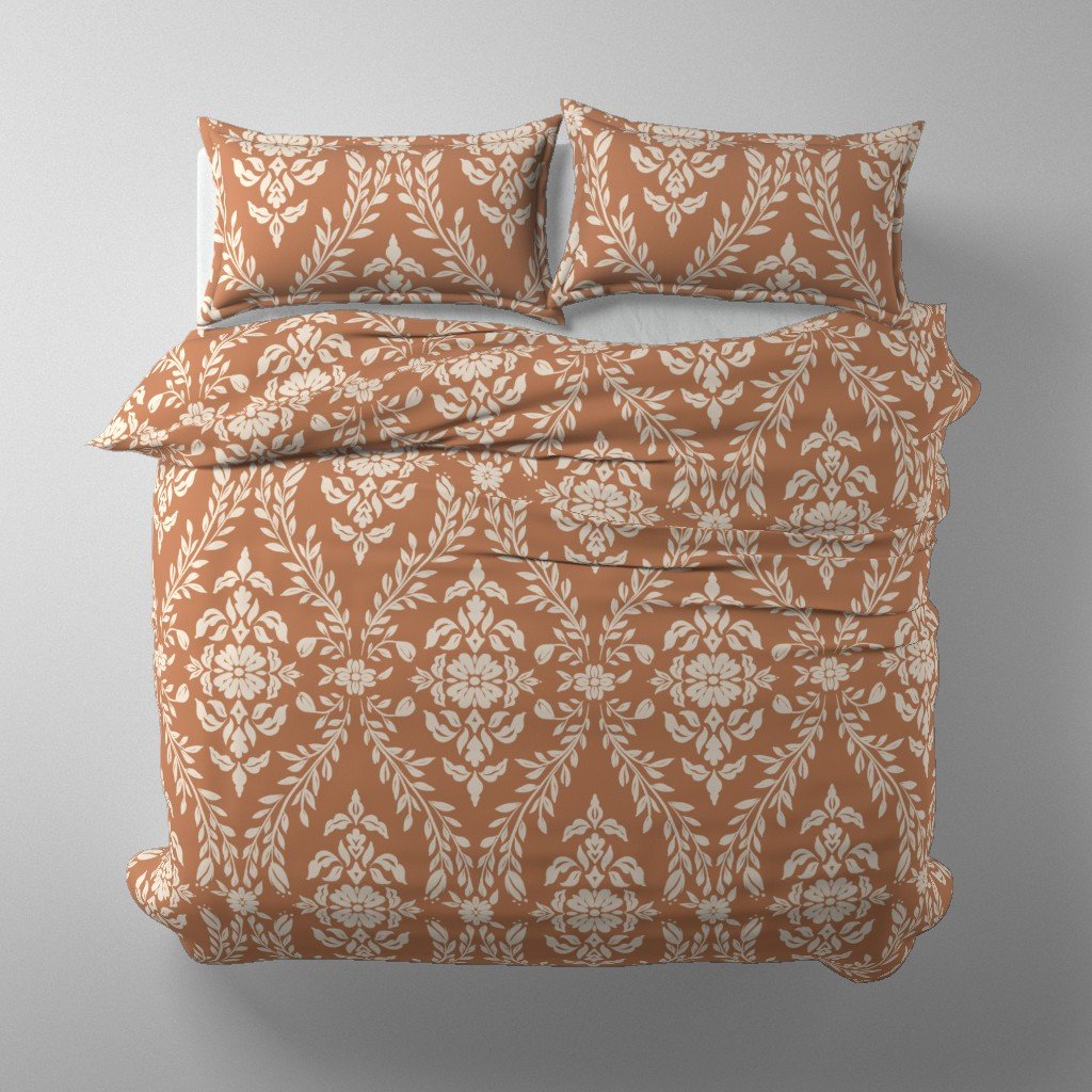 A bed with a terracotta and sand floral damask patterned comforter and matching pillows on a plain light gray background.