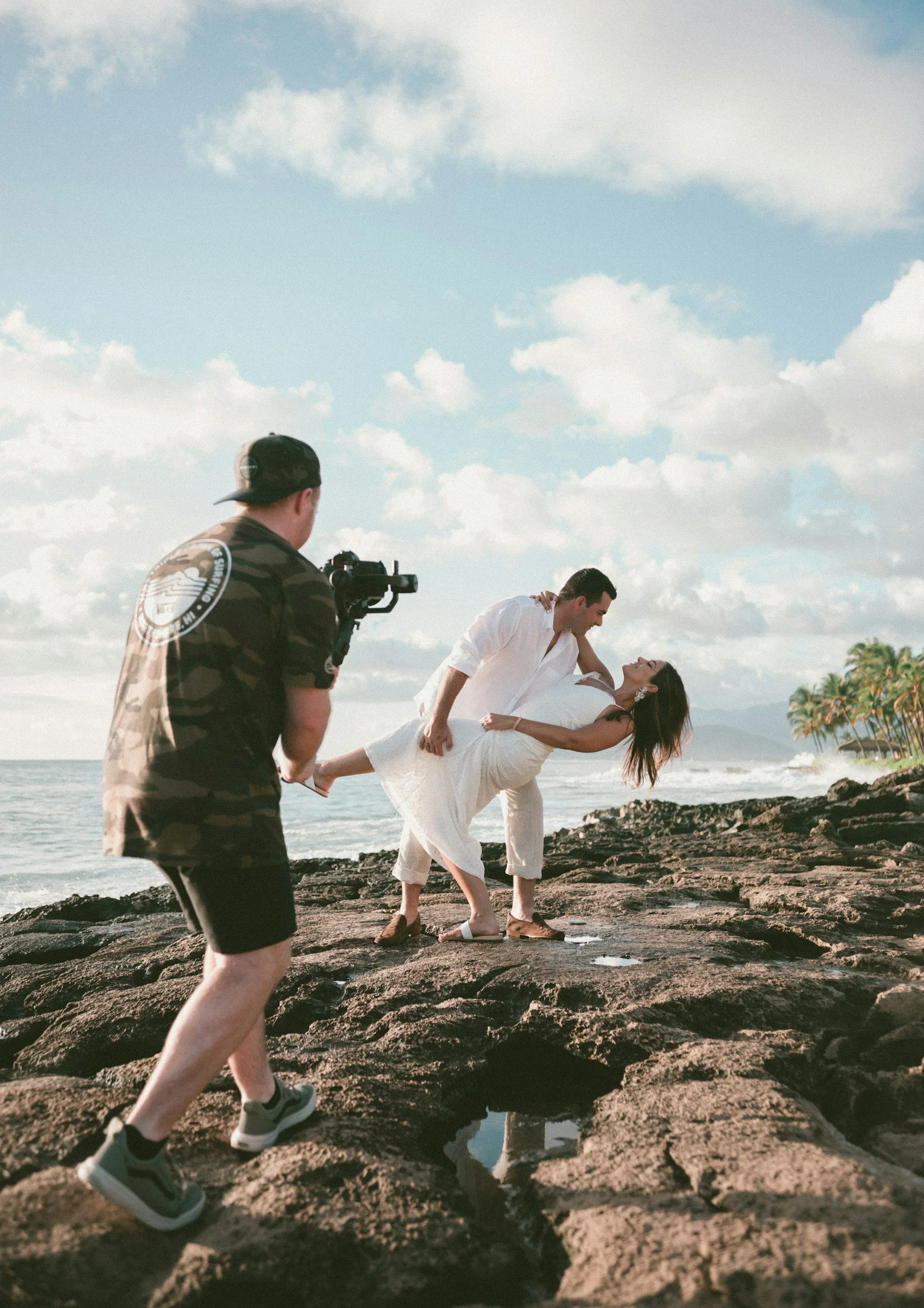 Elopement videographer capturing couple's romantic dip on oceanfront rocks