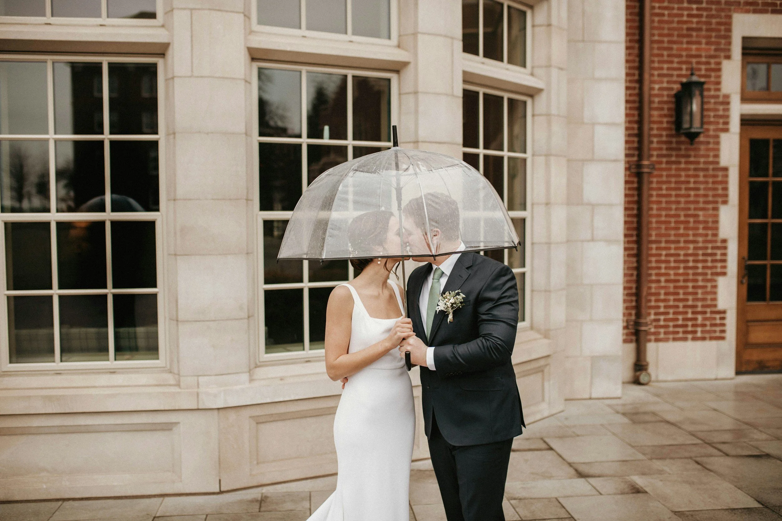 Wedding couple sharing a moment under clear umbrella outside of their ceremony