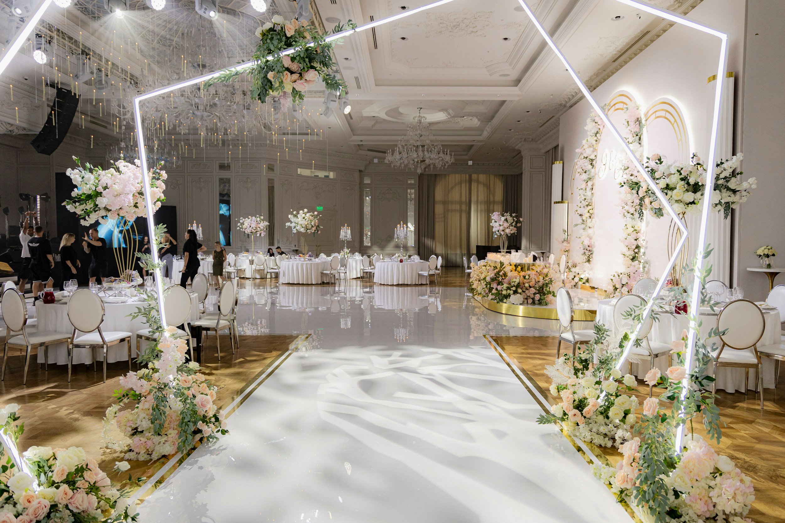 Elegant wedding reception in ballroom, blush and ivory florals, greenery, white linens, gold chairs, lit hexagon arch