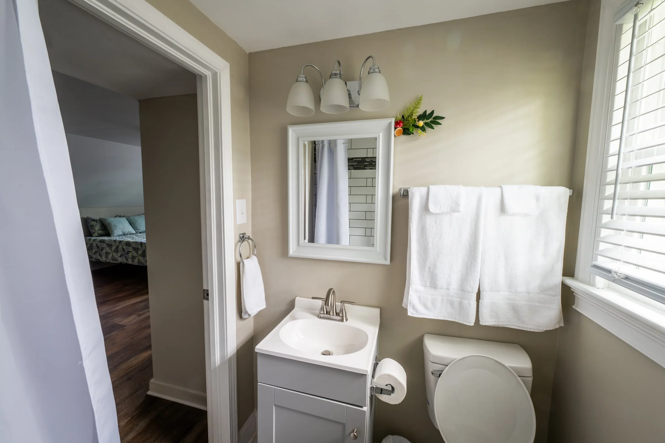 Small bathroom with a white sink, mirror, white towels, and a bathroom window with blinds.