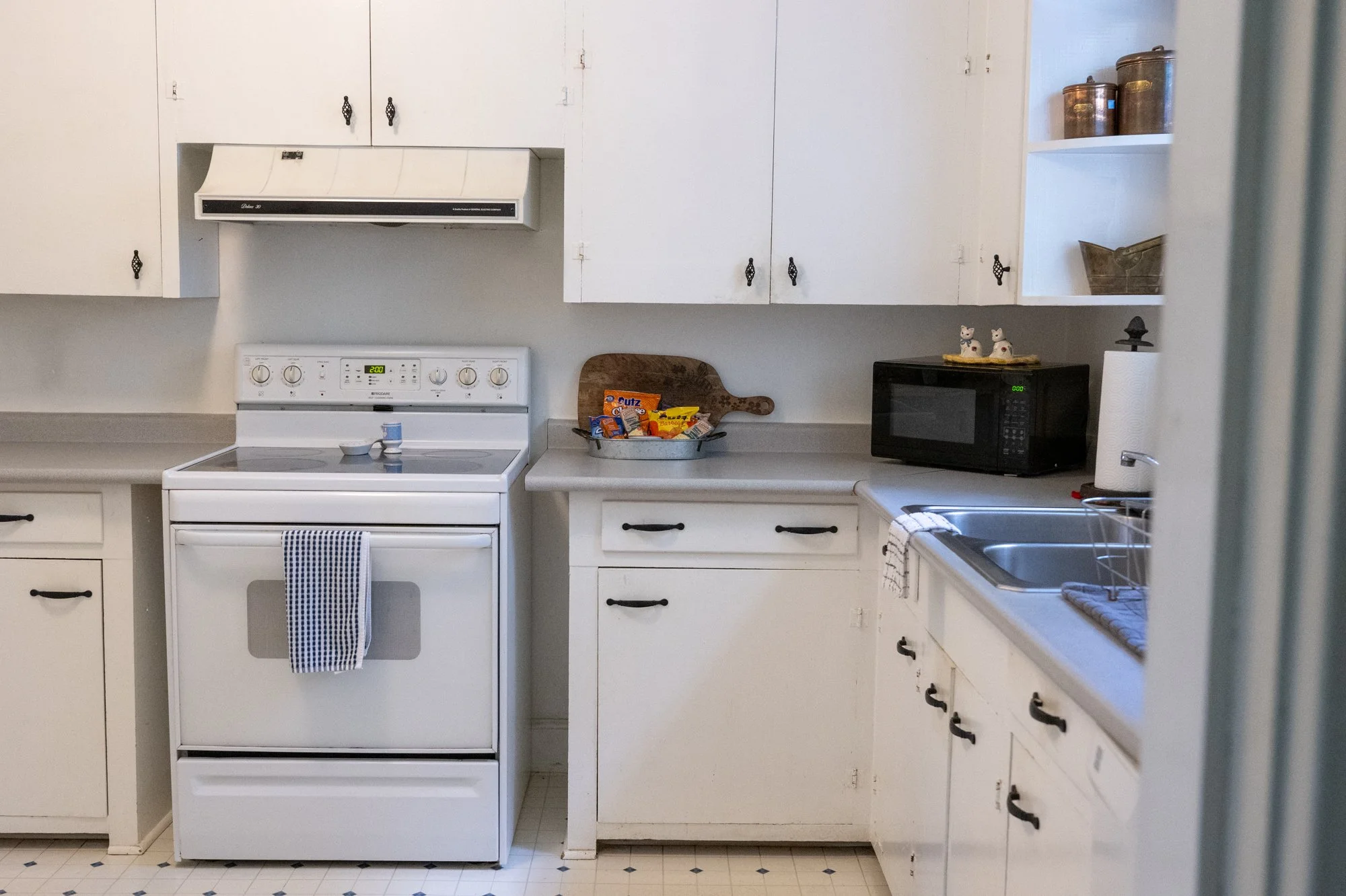 A kitchen with white cabinets, a white stove, a microwave, and a sink.