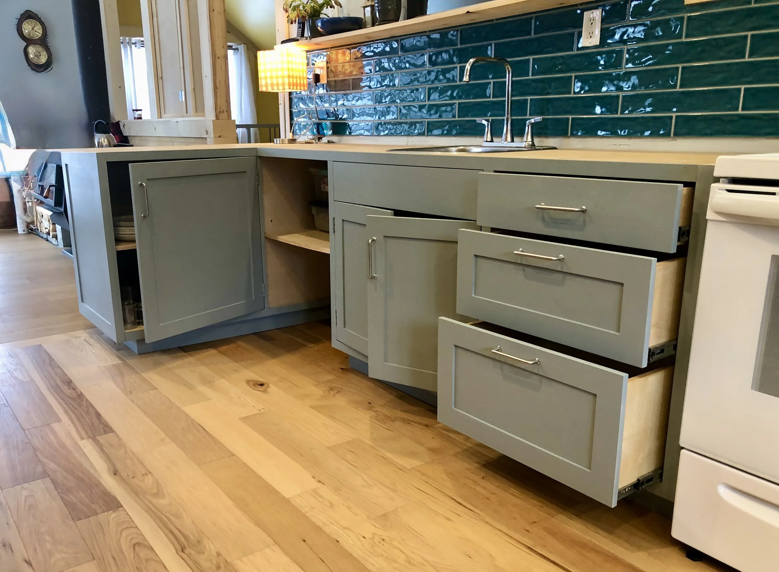Custom kitchen in Shaker style. Built with FSC Canadian birch plywood and solid pine doors, drawer fronts and face frames. Tile backsplash in teal and wavy texture to provide high sheen and water feel.  The floors are engineered hardwood made for dam