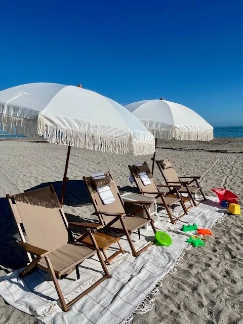 Beach chairs and white umbrellas on sandy beach with water in the background.