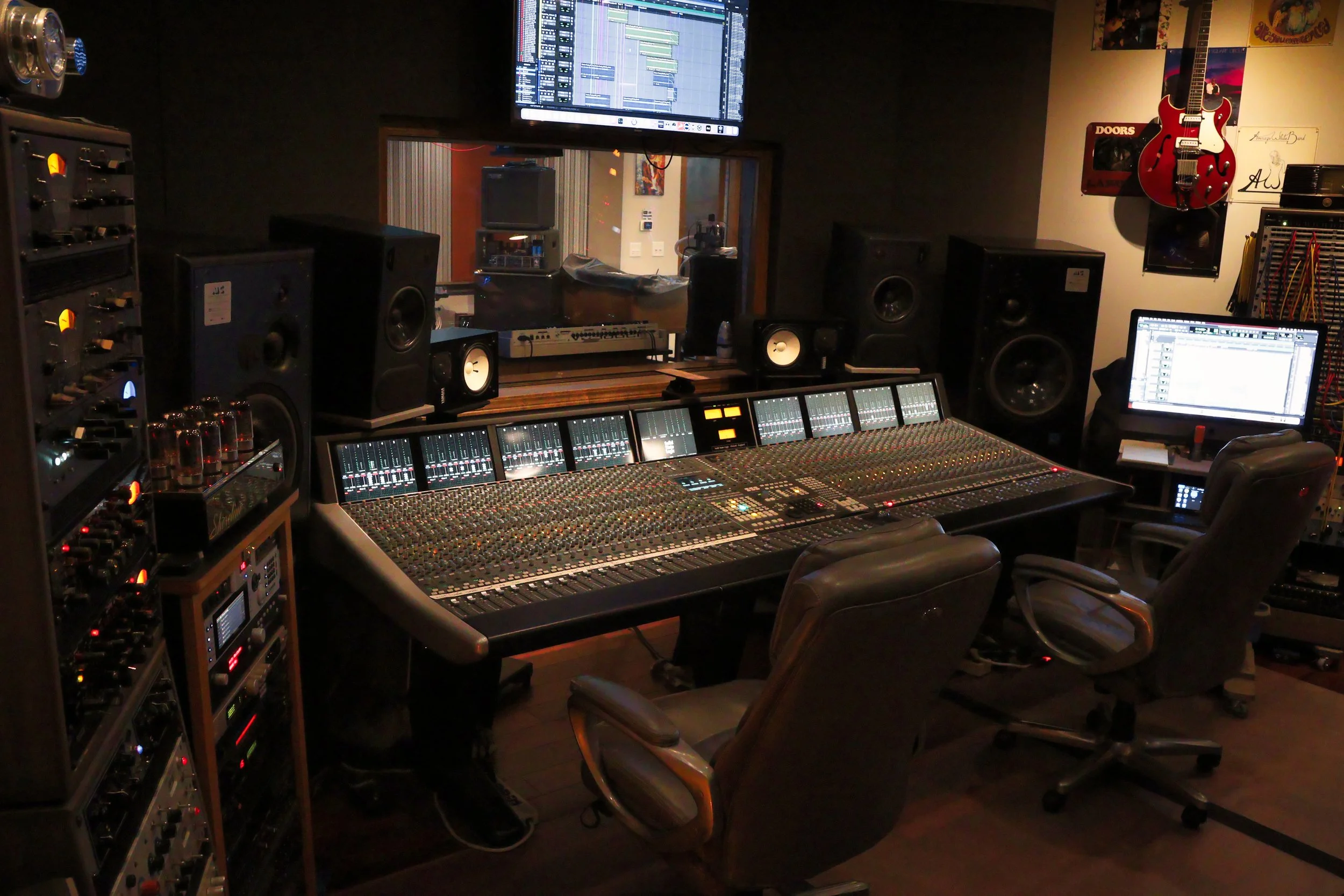Recording studio control room with mixing console, speakers, computer screens, guitar, and music posters