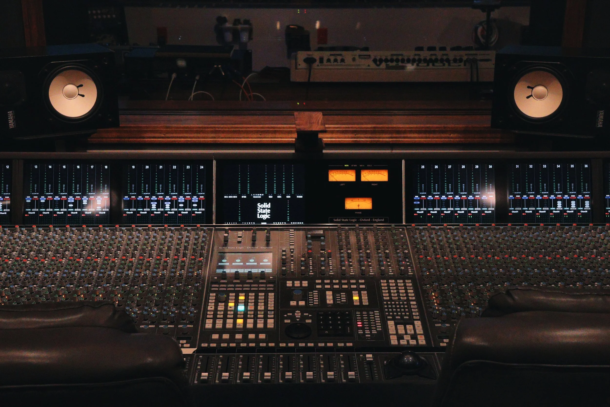 A professional audio mixing console with numerous controls, sliders, and meters, situated in a recording studio.
