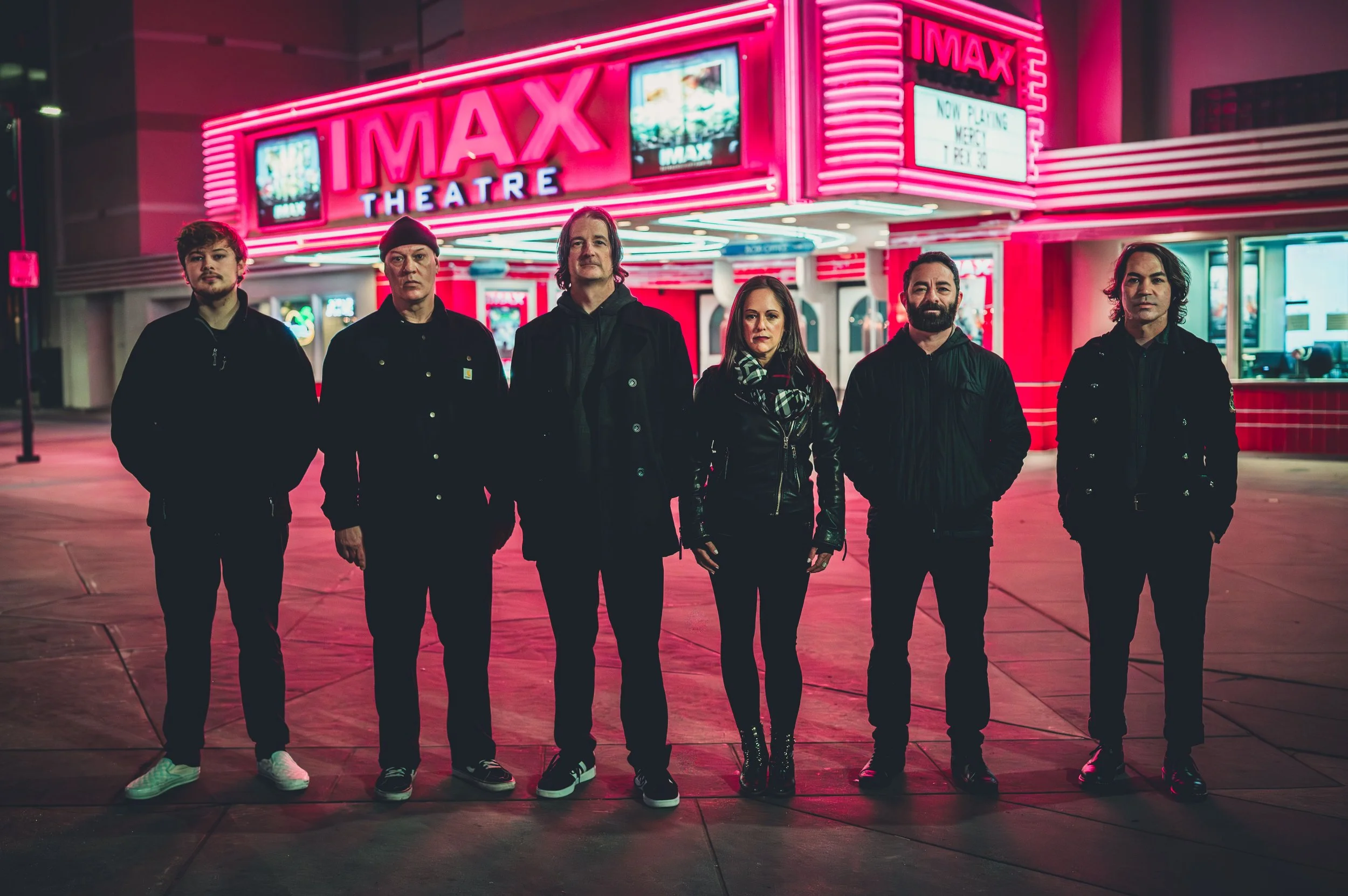 Six people standing in front of a bright pink neon-lit IMAX theater at night.
