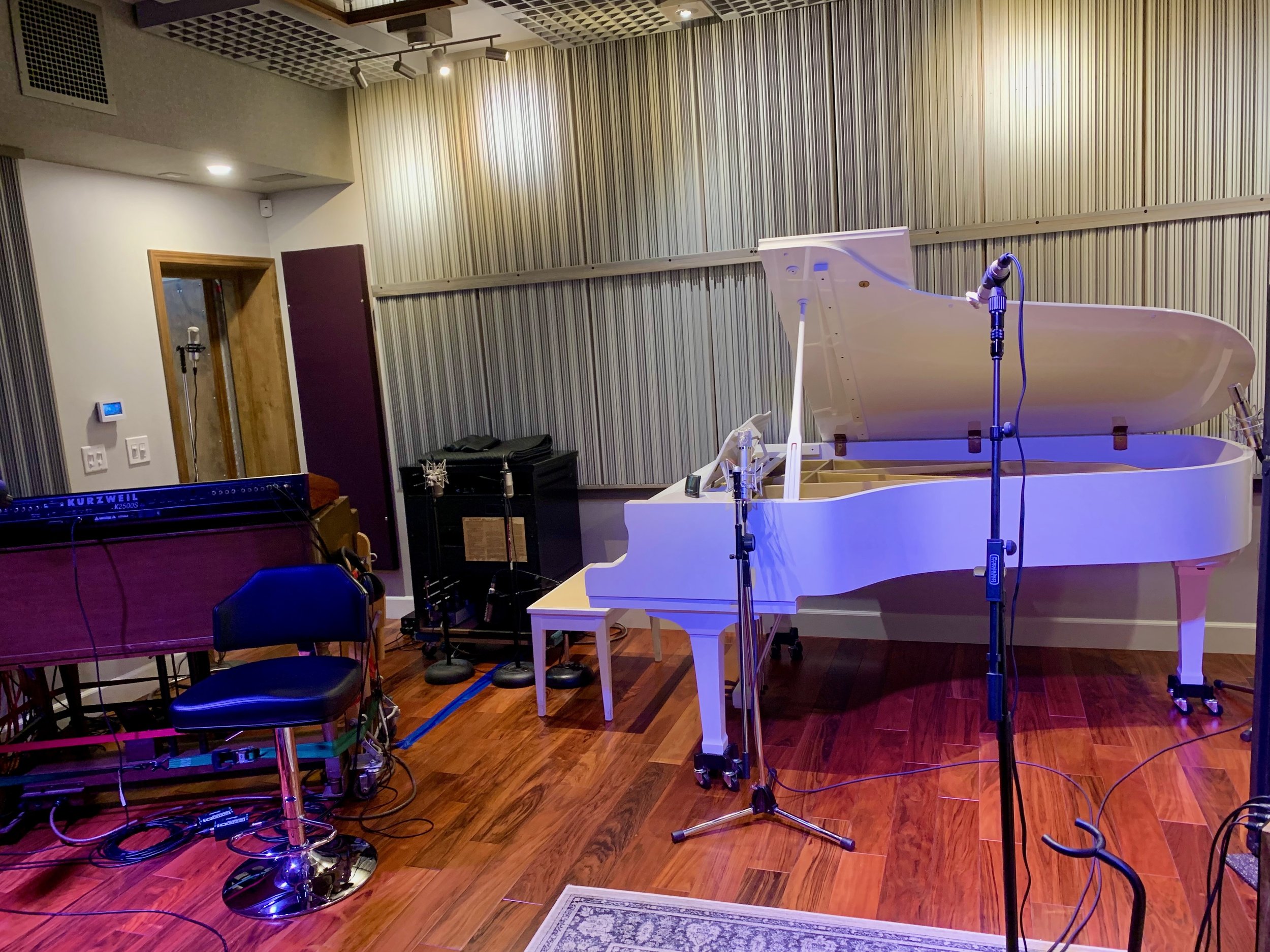 Recording studio with a white grand piano, microphones, music equipment, black chairs, and soundproofing walls.